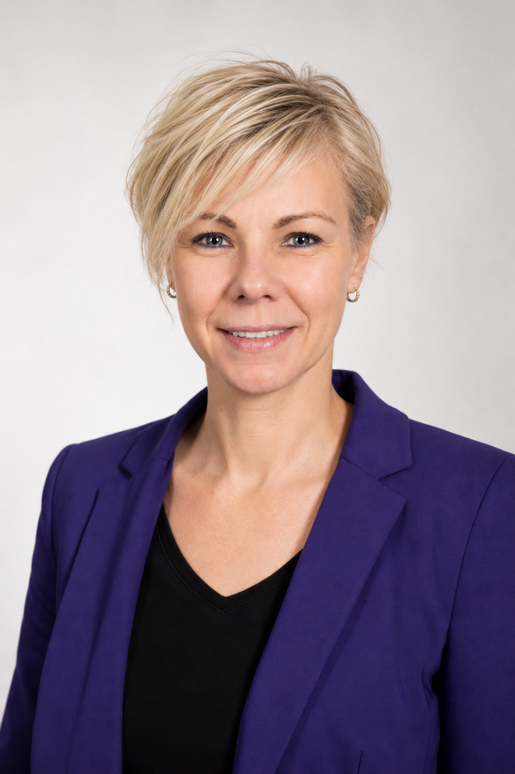 Porträt einer lächelnden Frau mit kurzem blondem Haar, schwarzem Top und blauer Blazer vor weißem Hintergrund. Die Frau ist Ilka Cirkel und arbeitet bei der BUGA31.