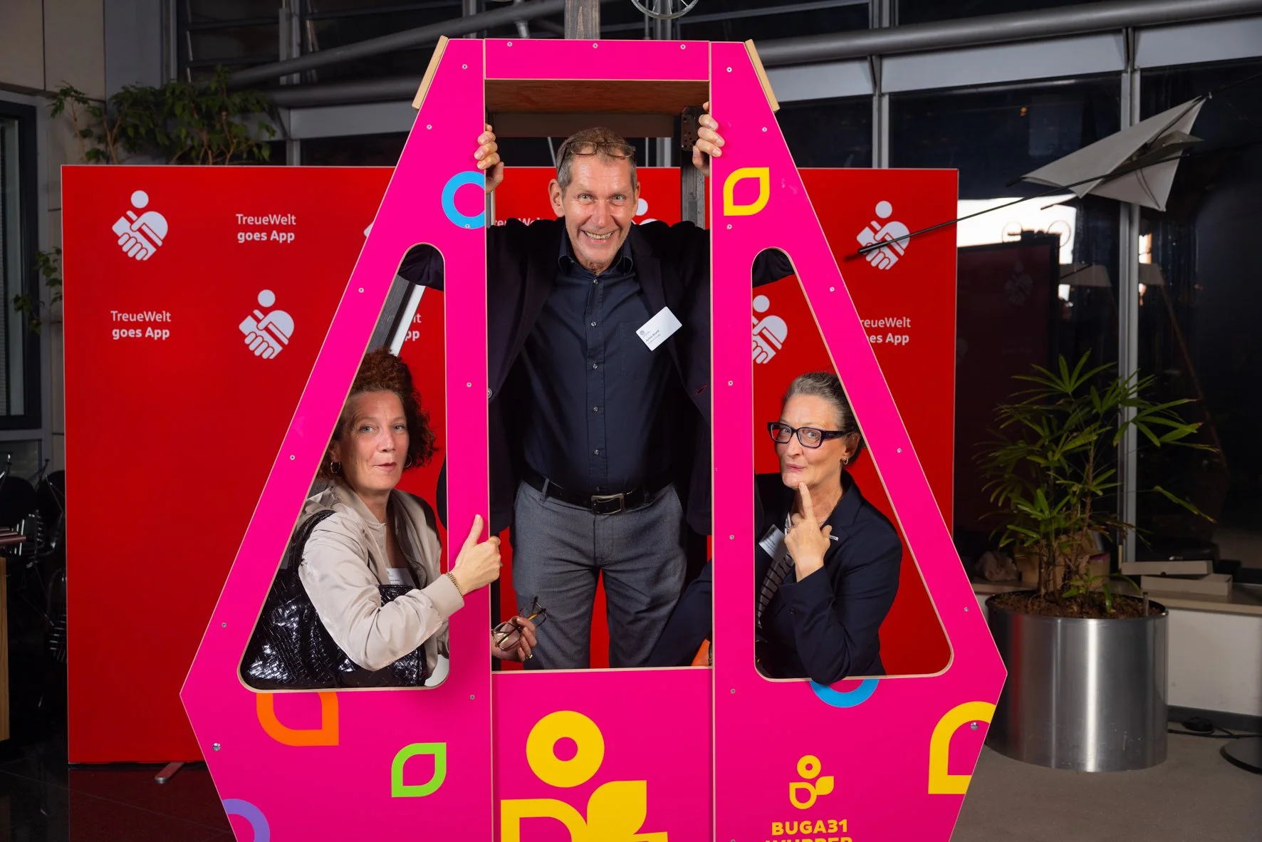 Drei Frauen und ein Mann posieren in einem Fotokasten bei einer Veranstaltung. Die Frauen schauen nach vorne und der Mann lächelt in die Kamera.