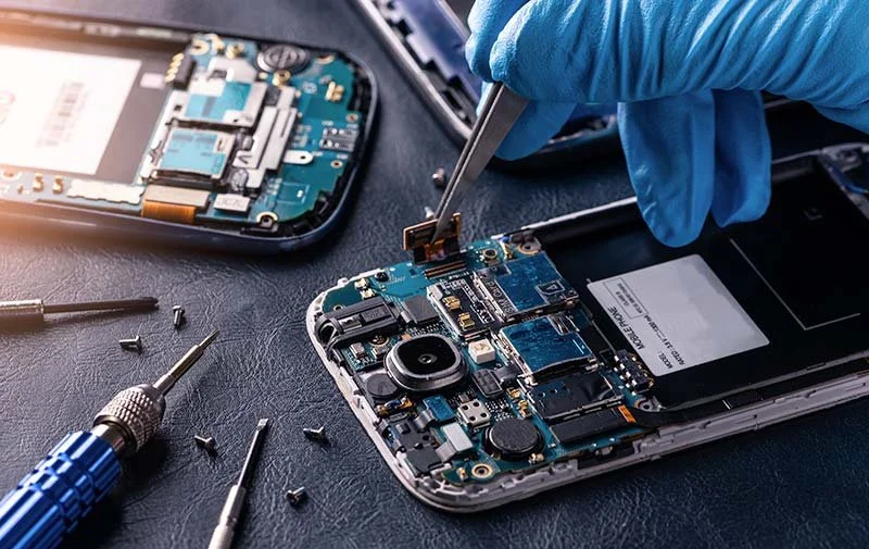 Close-up view of a technician repairing a smartphone by replacing internal components with tools, including a screwdriver and tweezers.
