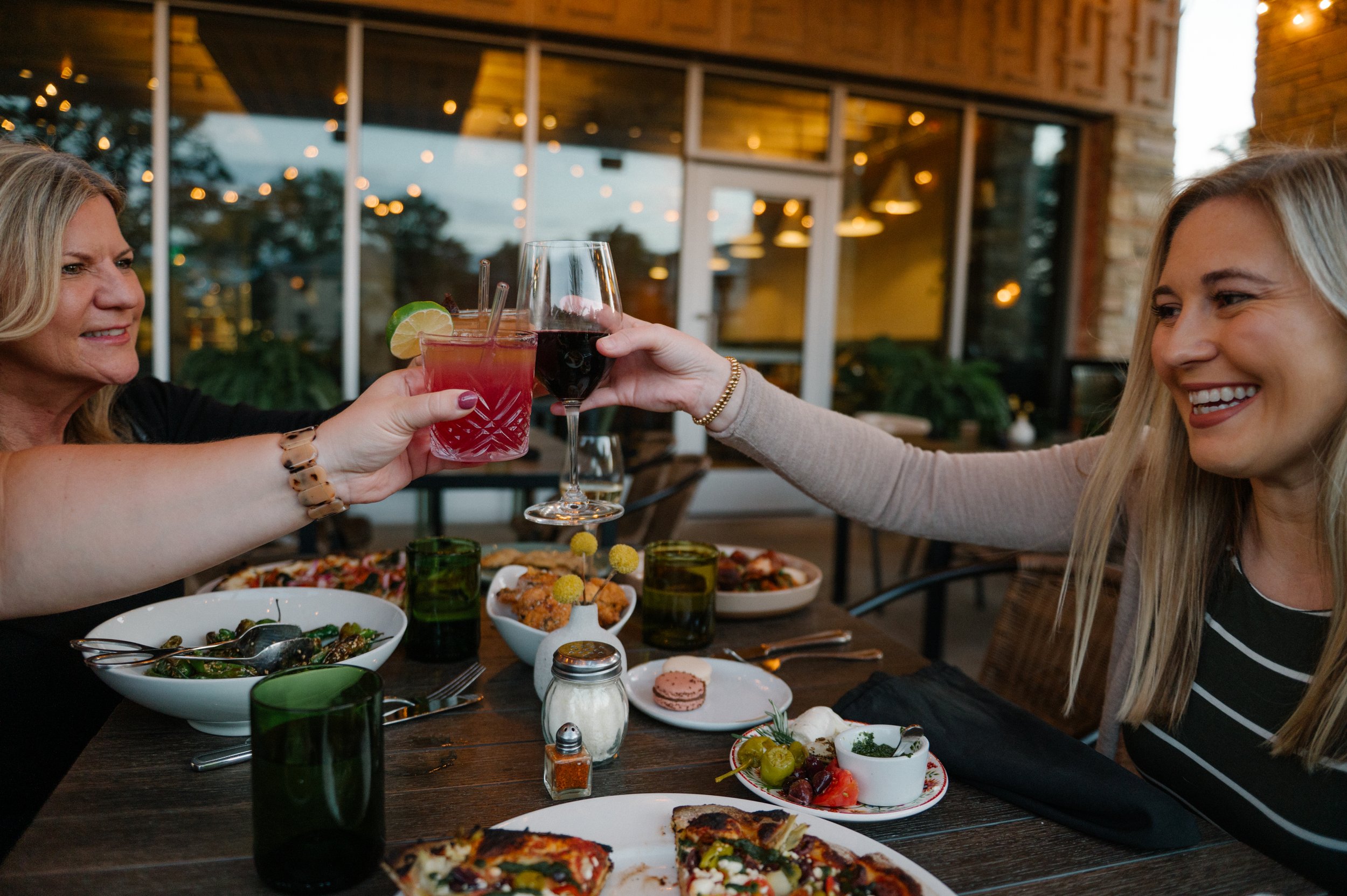 Guests dining on Hugo’s covered patio with wood-fired pizza and cocktails.