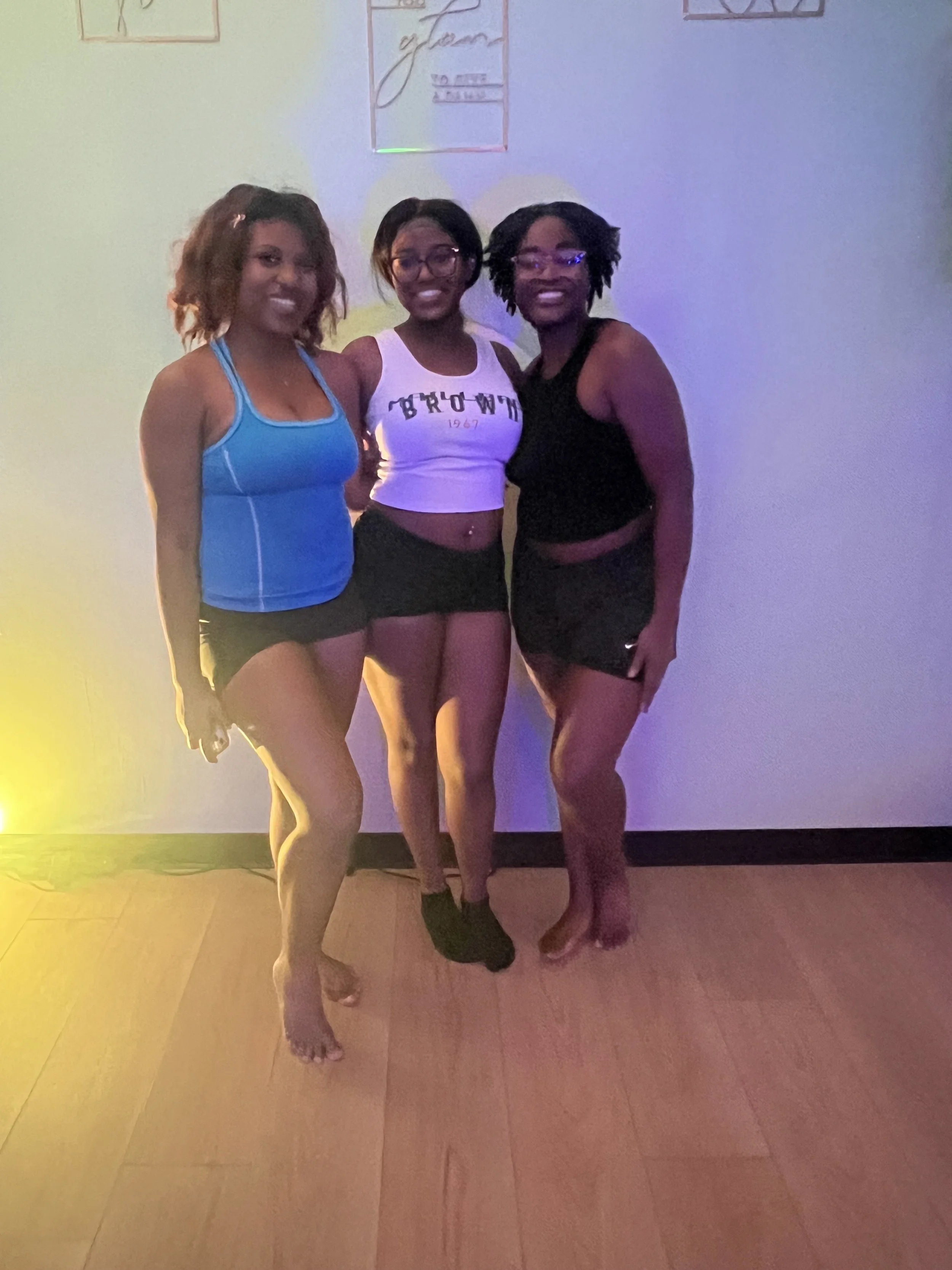 Three women standing close together, smiling for a photo in a room with colorful lighting and wall decorations.