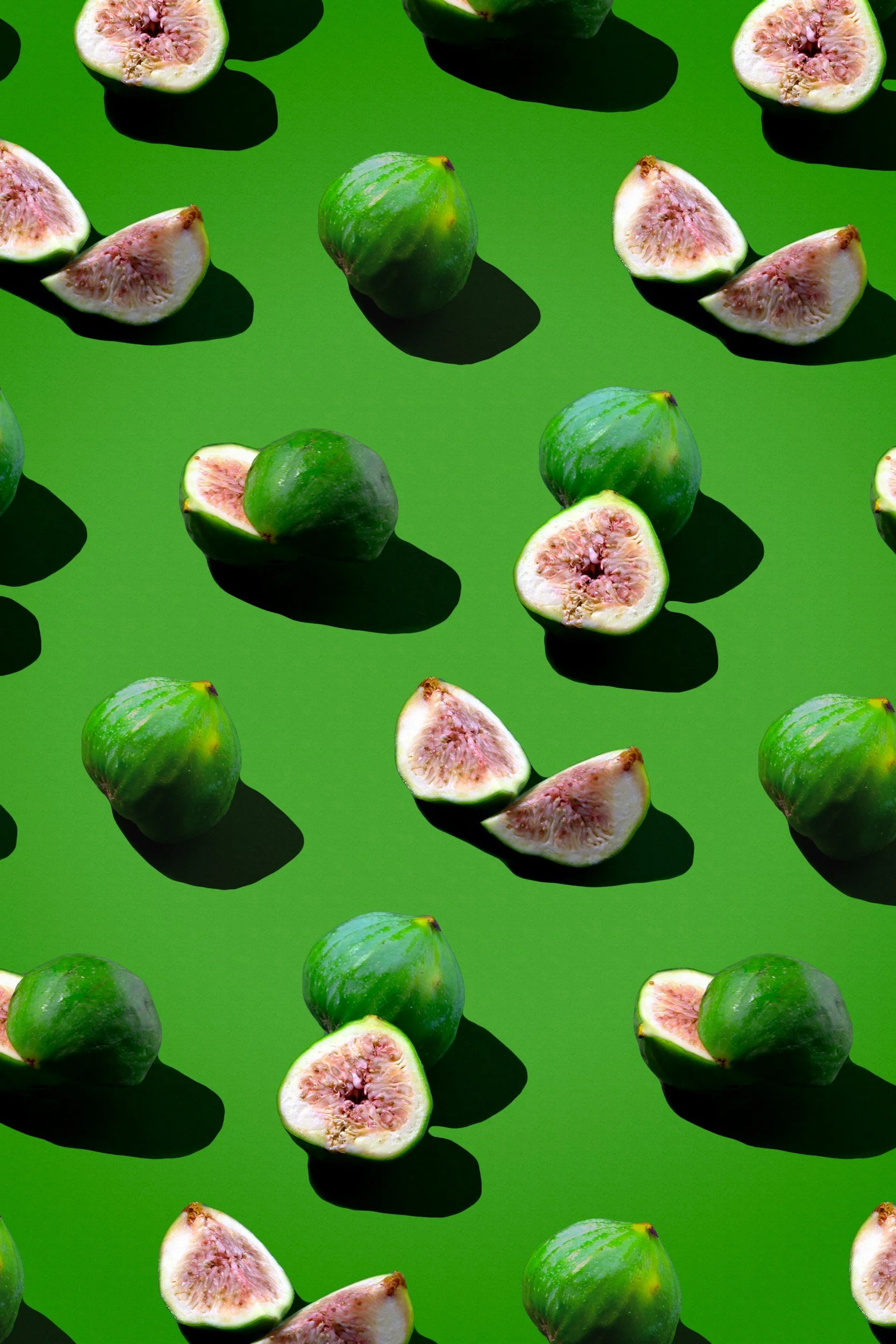 Fresh figs, whole and halved, arranged on a bright green background.