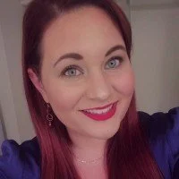 Woman with long brown hair smiling, wearing red lipstick and a purple outfit.