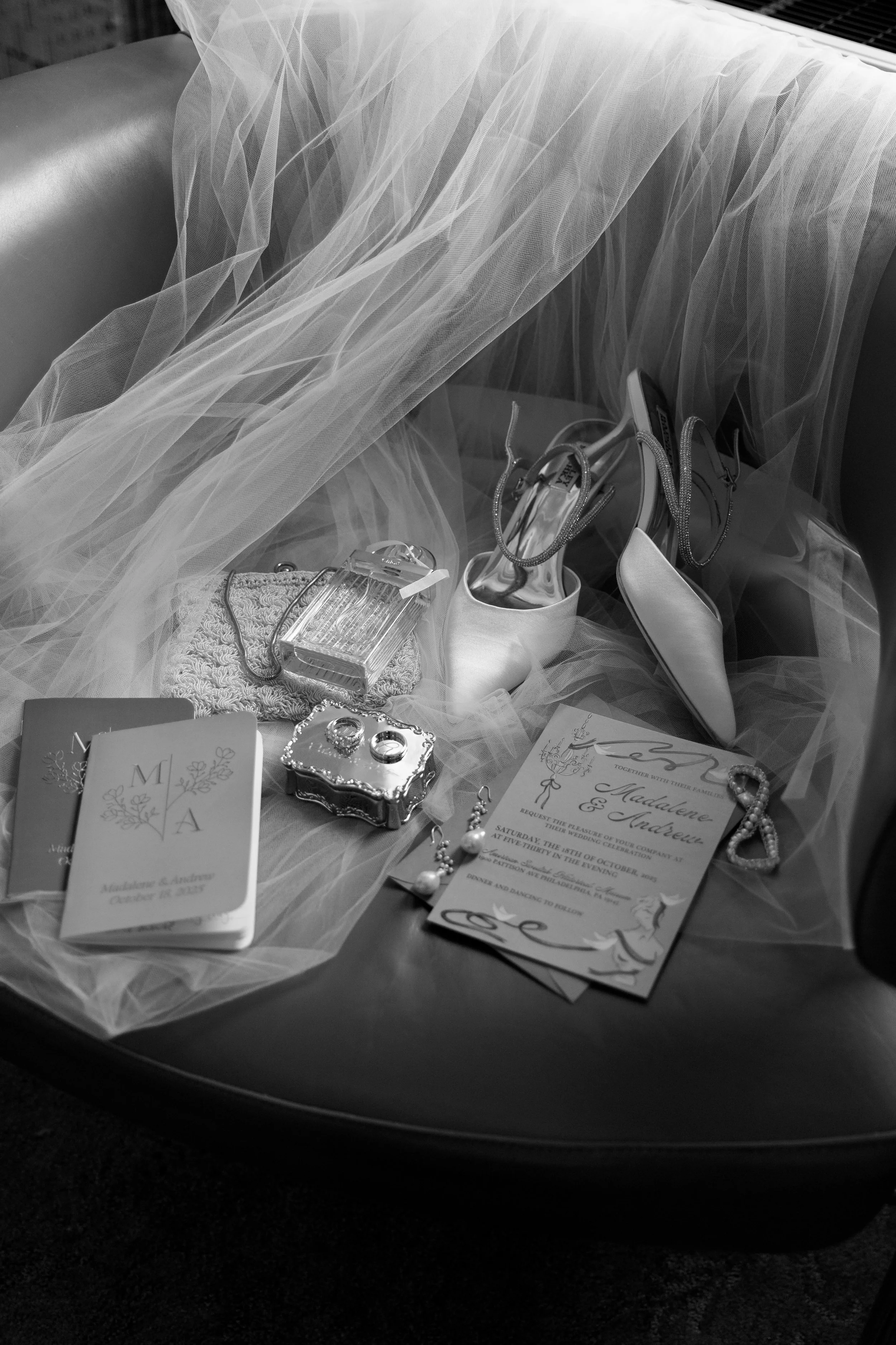 Wedding accessories and invitations arranged on a round table, including a veil, high heels, jewelry, a purse, and a wedding invitation for Madeleine and Andresen.