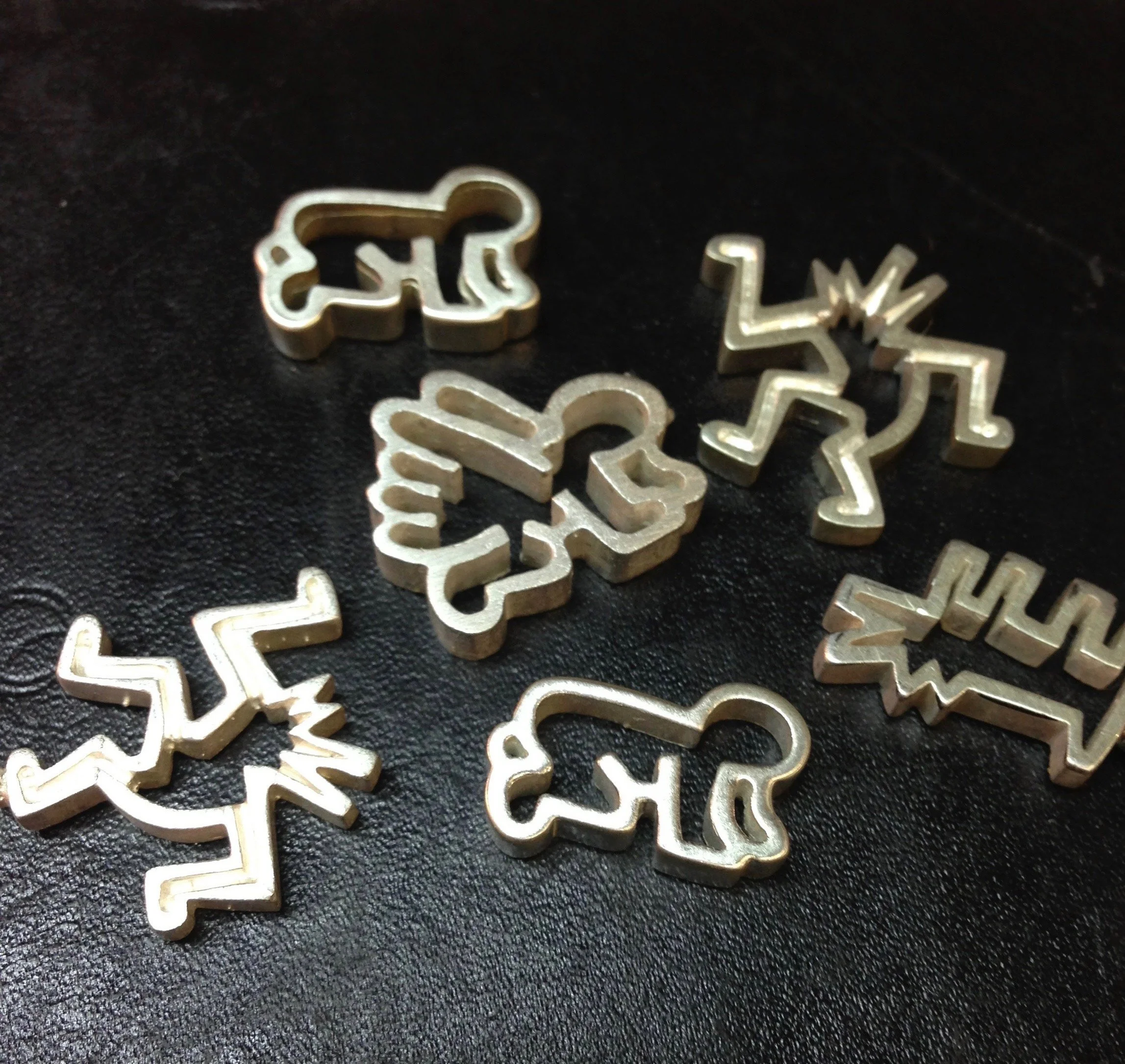 Several small metal cookie cutters in the shape of reindeer and Christmas trees on a black surface.