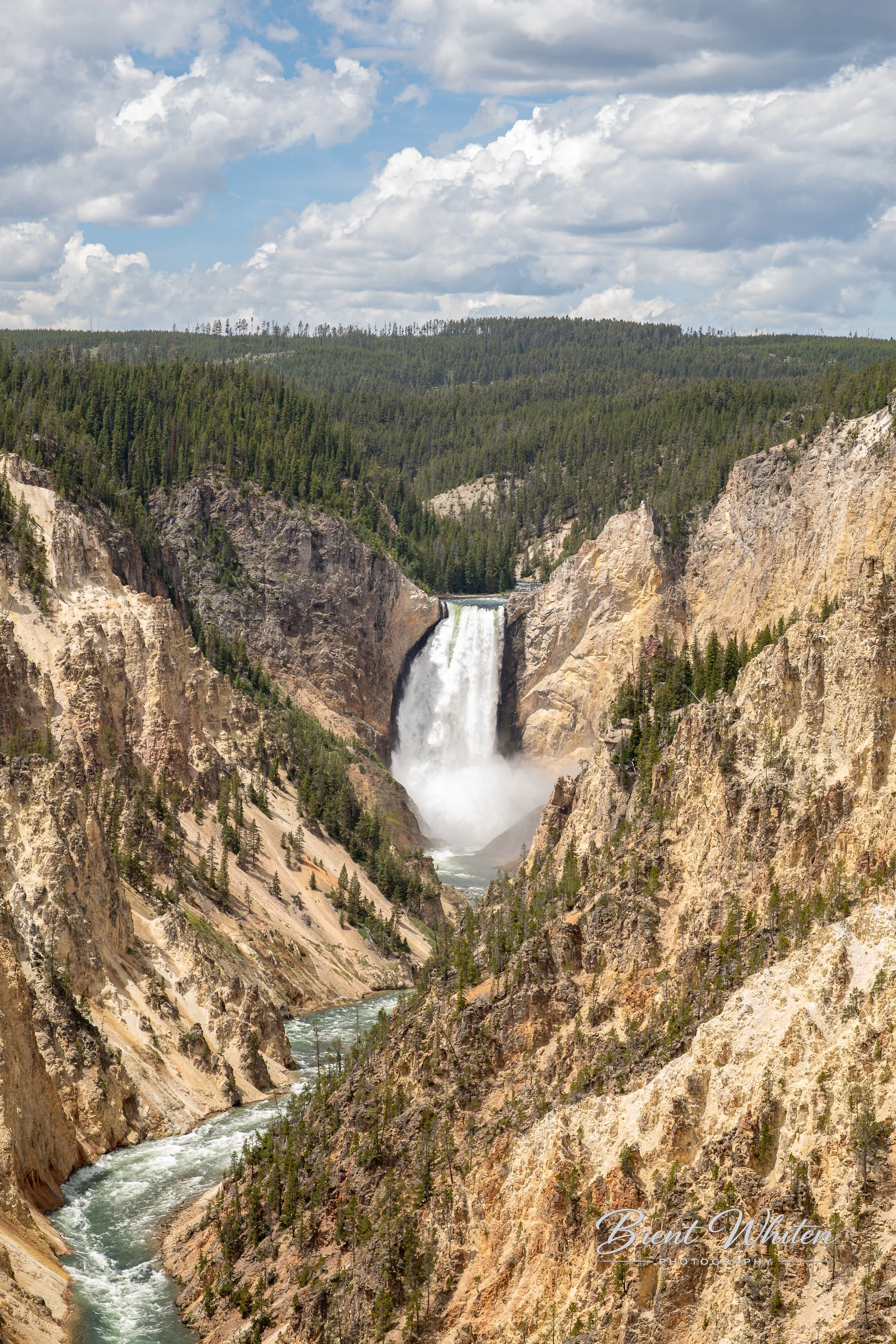Waterfall flowing through a canyon with rocky cliffs and green forest, cloudy sky overhead.