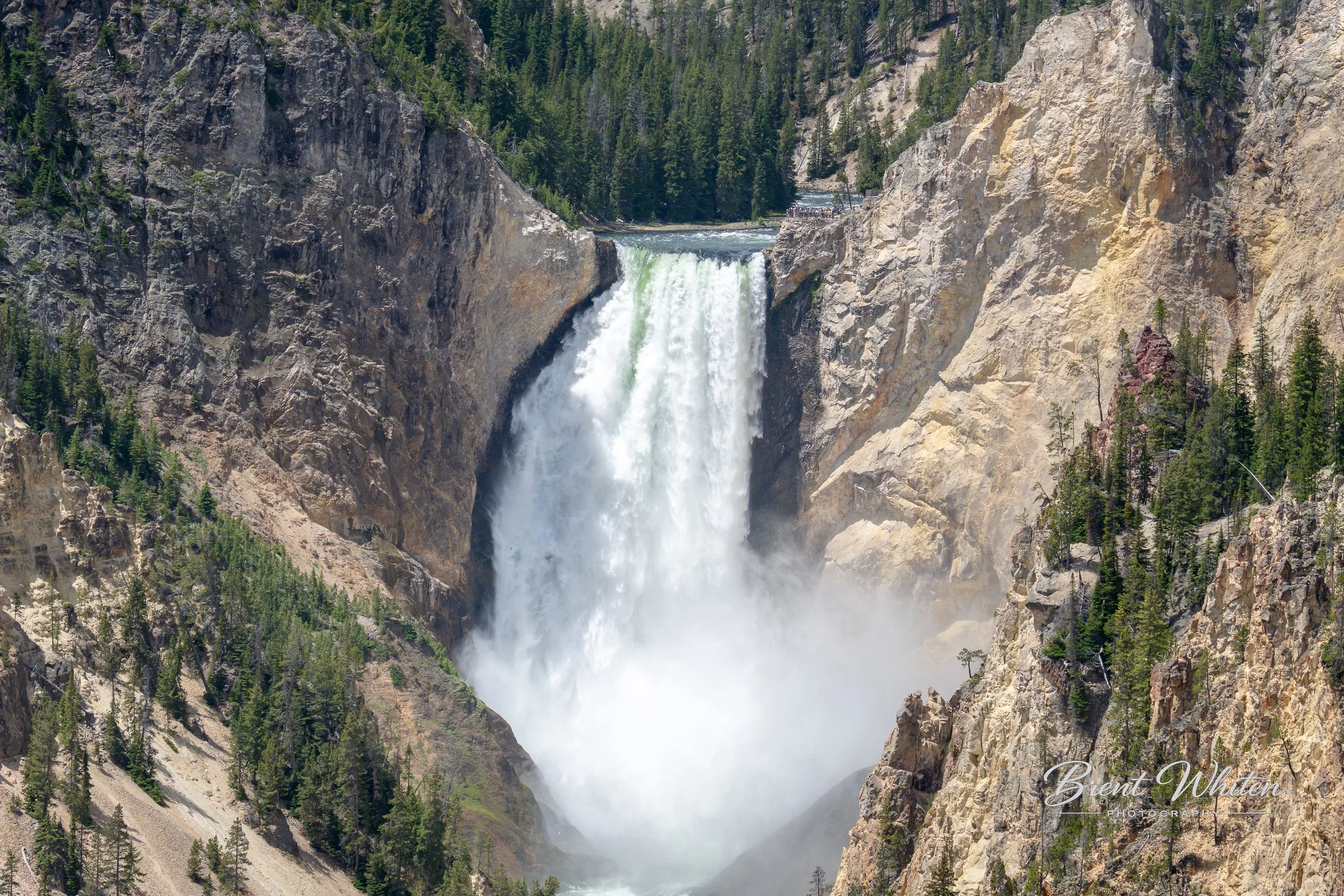 A large waterfall flowing through rocky cliffs with evergreen trees surrounding it.