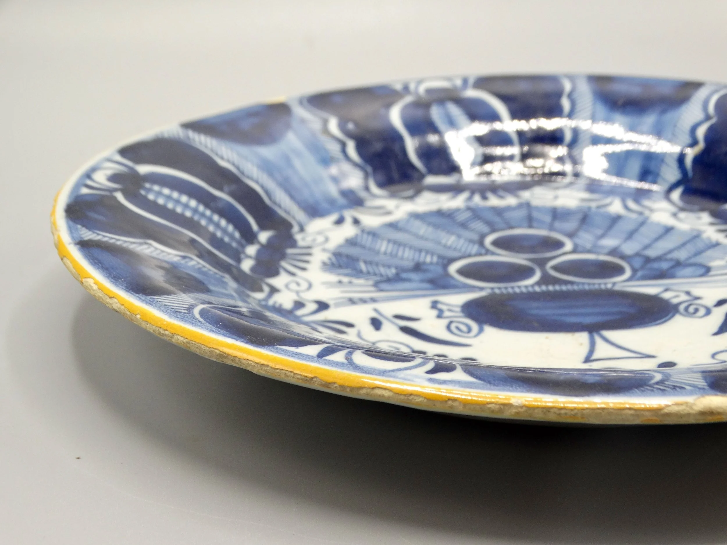 Ochre rim and stylized flower heads on late 18th-century Dutch Delft peacock plate, Three Bells, De Drie Klokken