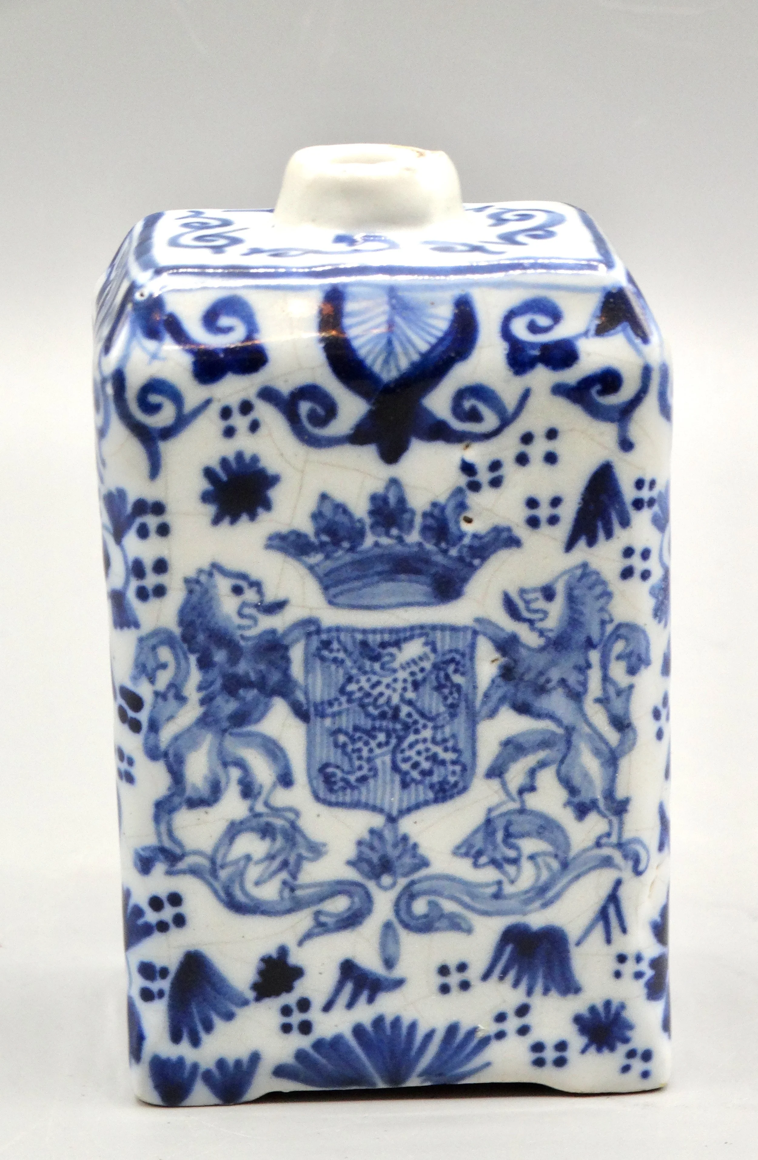 Close-up of hand painted rampart lions, crown, and floral decoration on 19th-century English Delft tea caddy.