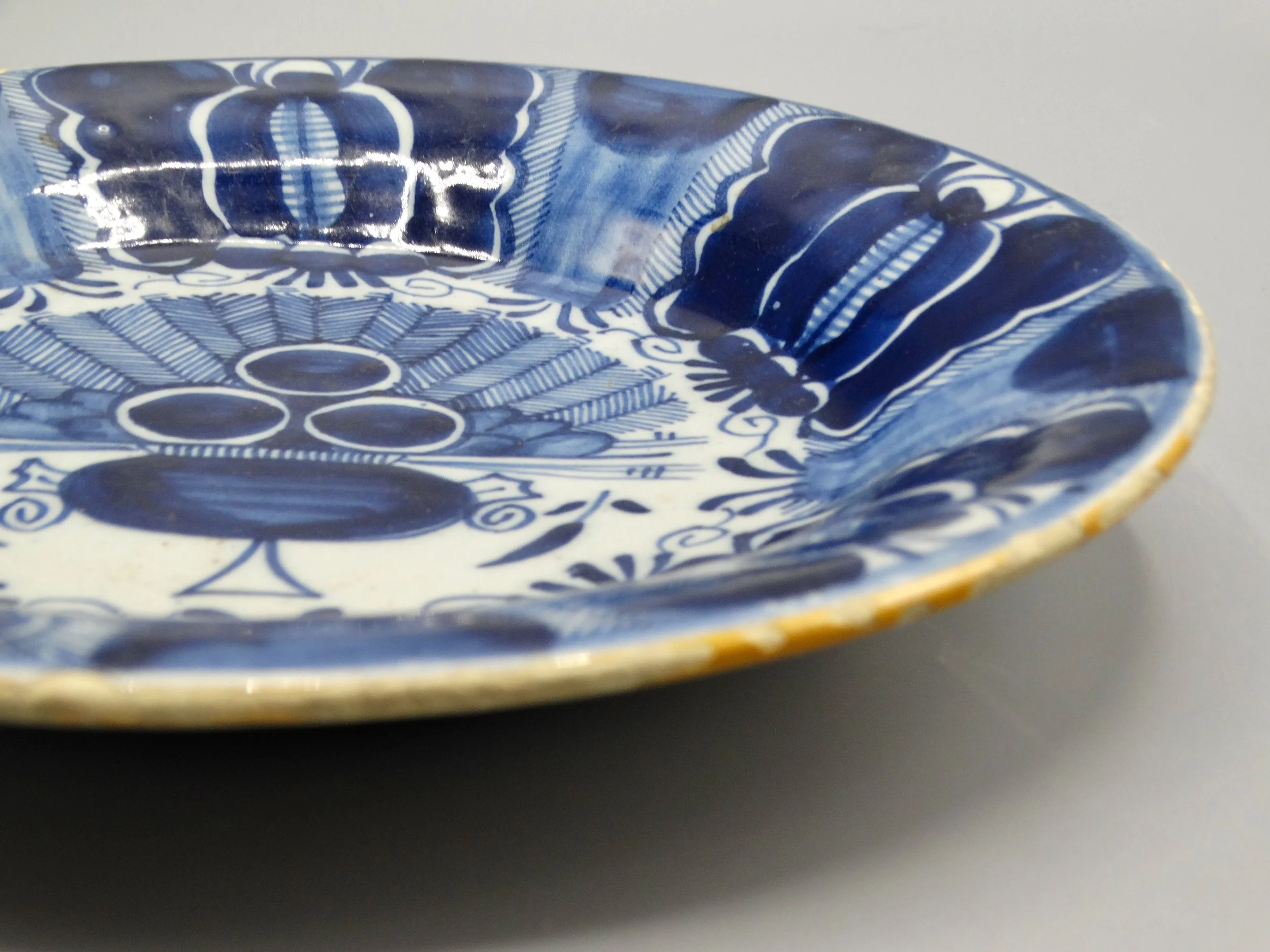 Ochre rim and stylized flower heads on late 18th-century Dutch Delft peacock plate, Three Bells, De Drie Klokken