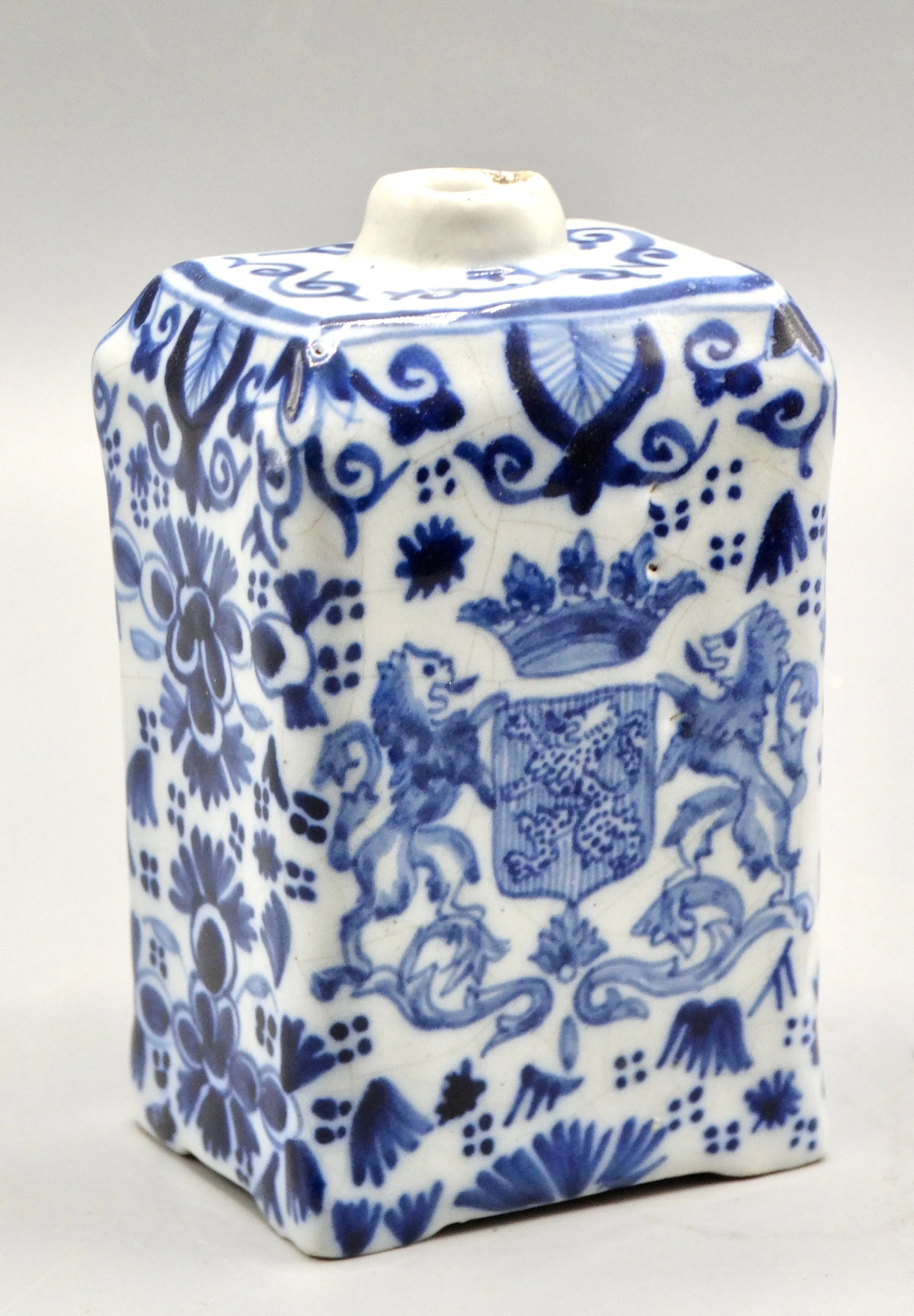 Close-up of hand painted rampart lions, crown, and floral decoration on 19th-century English Delft tea caddy.
