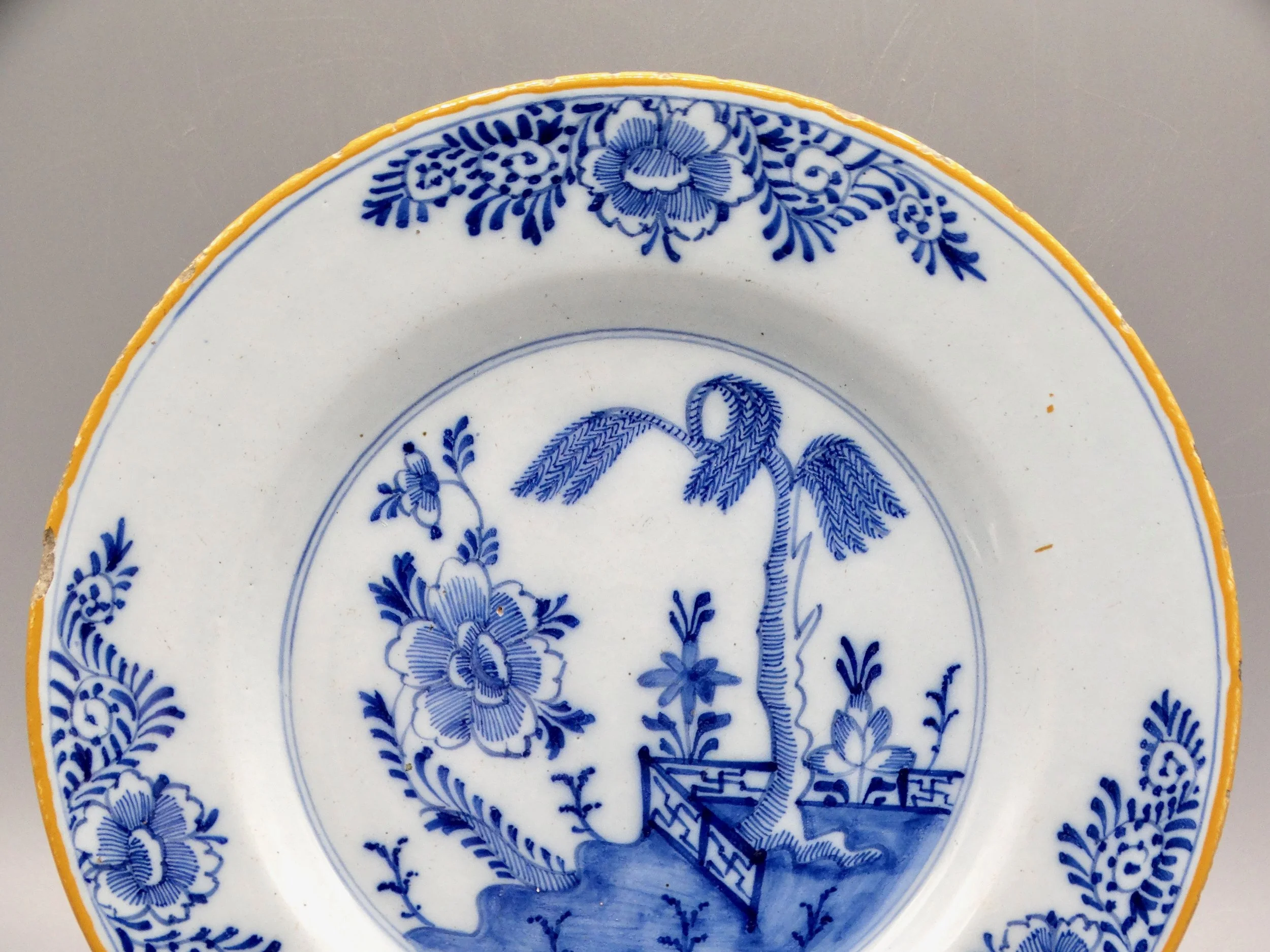 Orange-yellow border and geometric rim detail on 18th-century Dutch Delft chinoiserie plate.