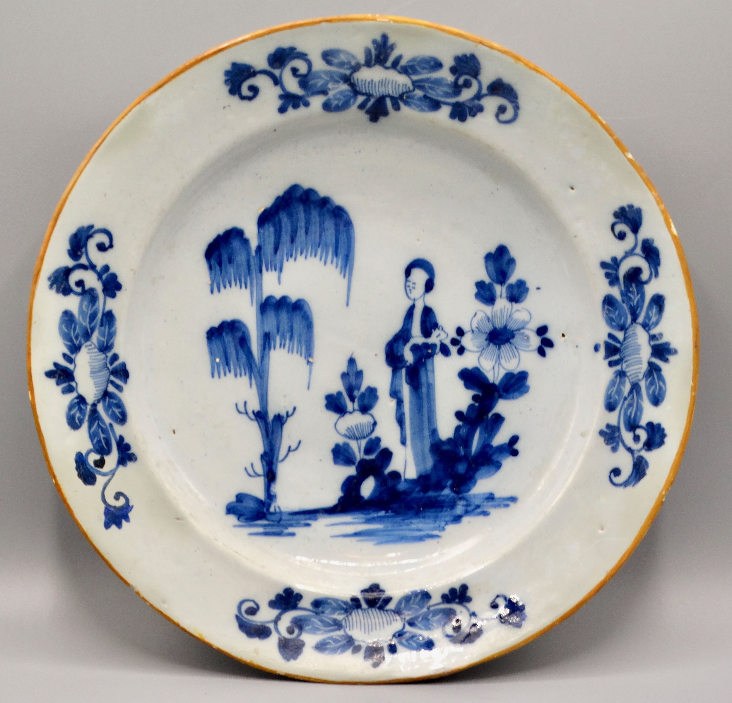 18th-century Dutch Delft figural charger “Lange Lijs” with hand painted blue design and orange edge.