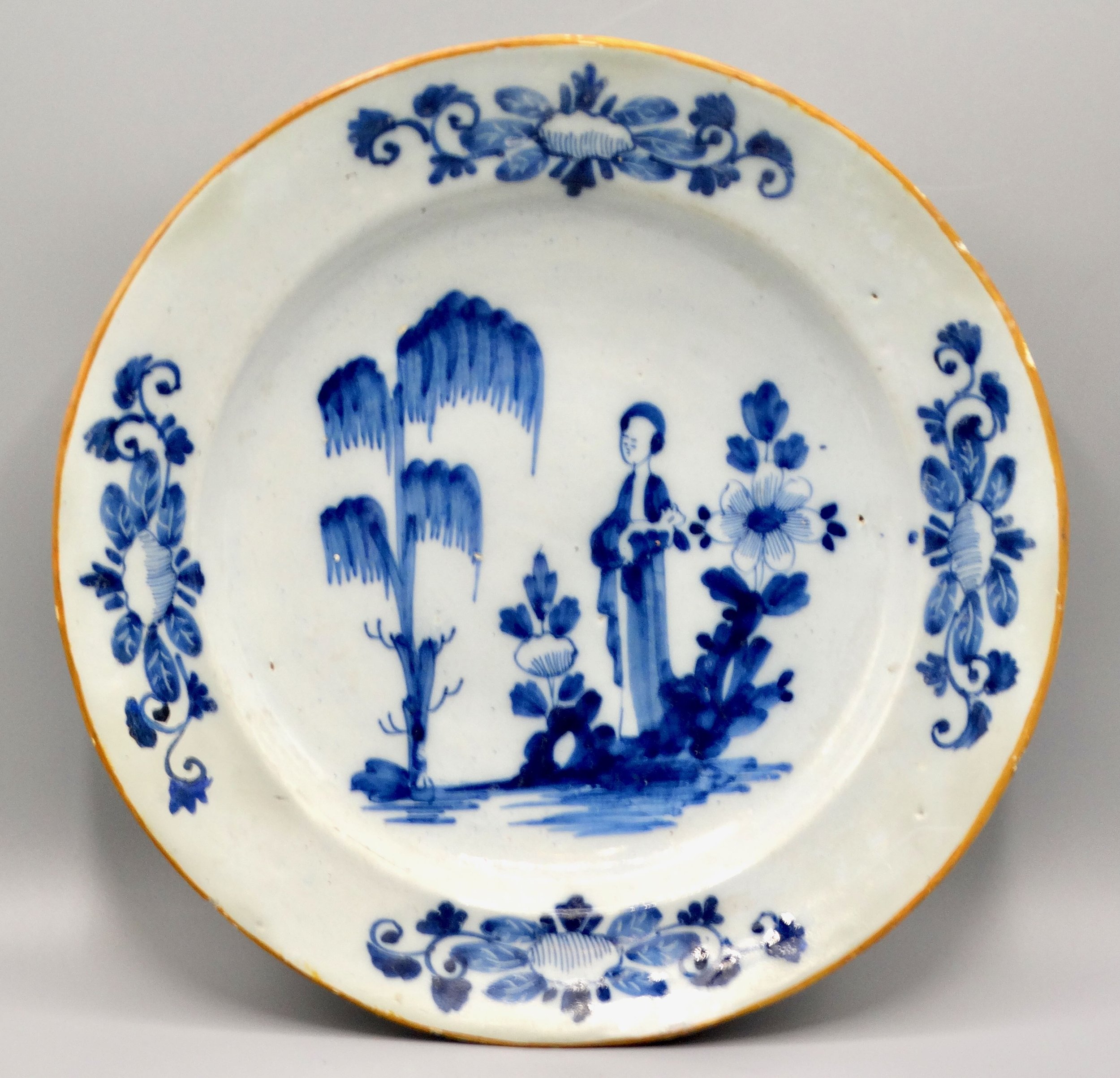 18th-century Dutch Delft figural charger “Lange Lijs” with hand painted blue design and orange edge.