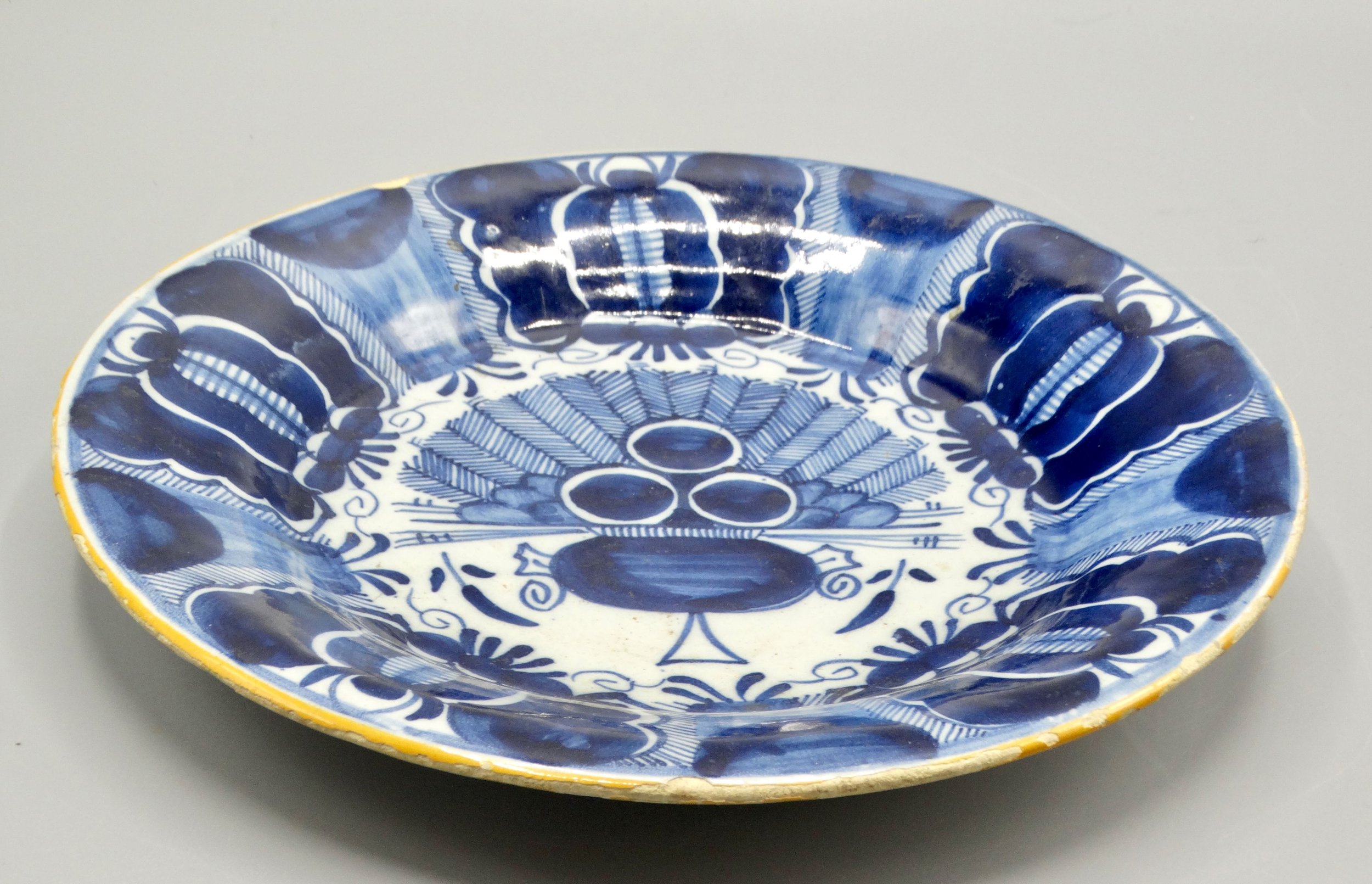 Ochre rim and stylized flower heads on late 18th-century Dutch Delft peacock plate, Three Bells, De Drie Klokken