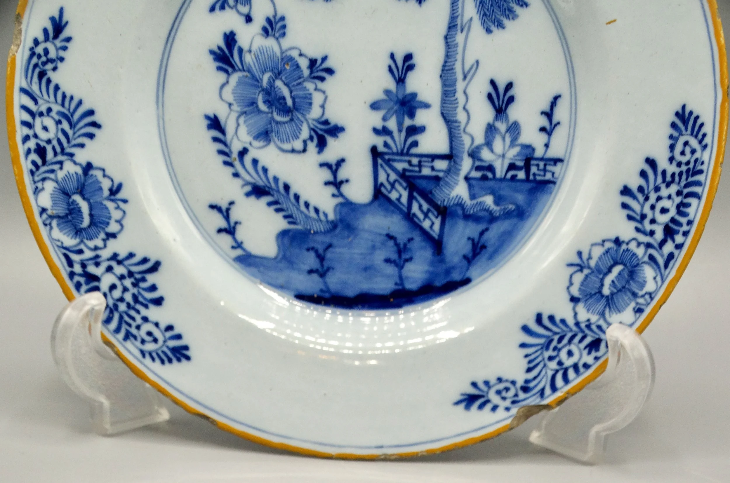 Orange-yellow border and geometric rim detail on 18th-century Dutch Delft chinoiserie plate.