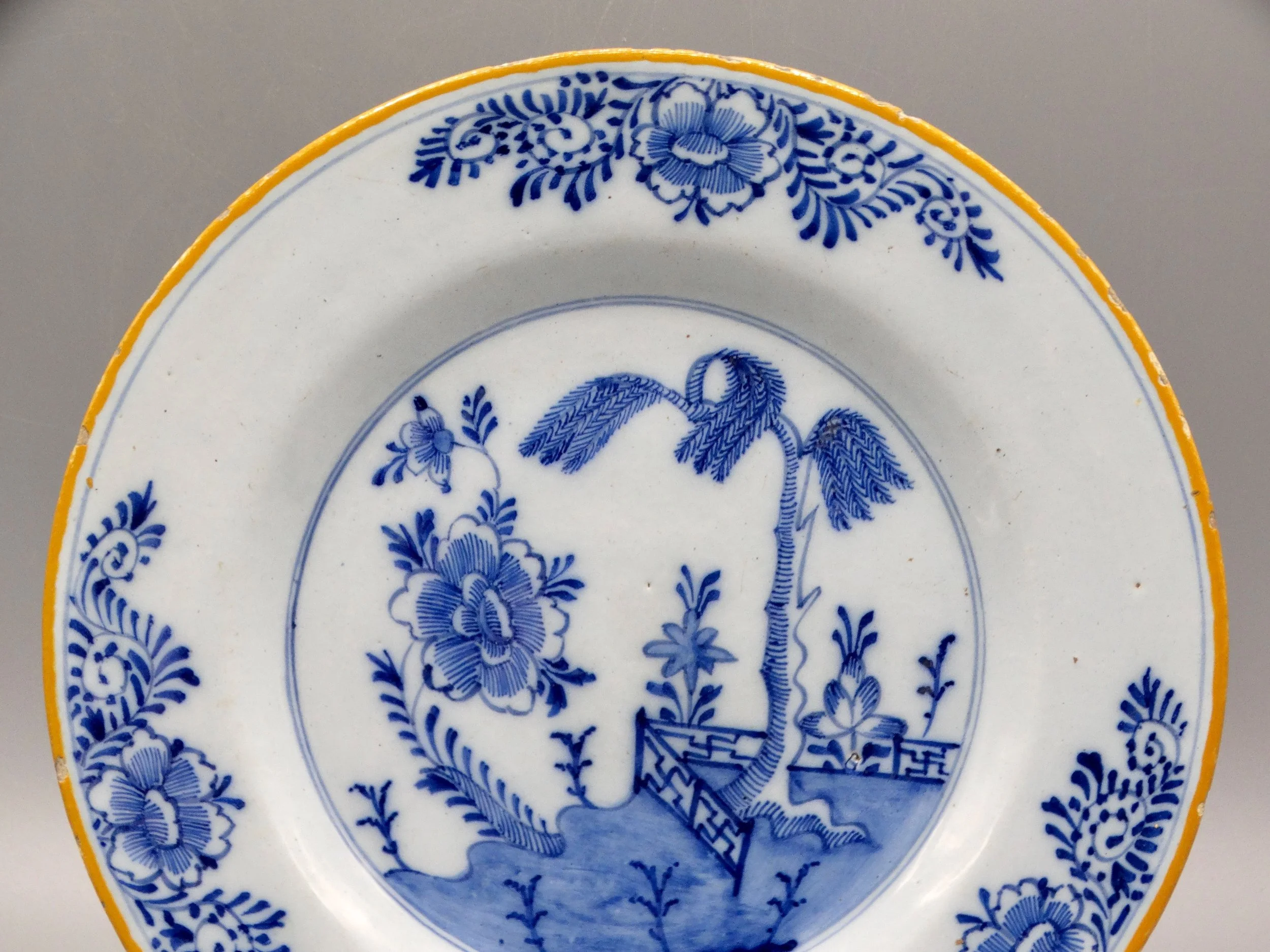 Orange-yellow border and foliate rim detail on second 18th-century Dutch Delft chinoiserie plate.