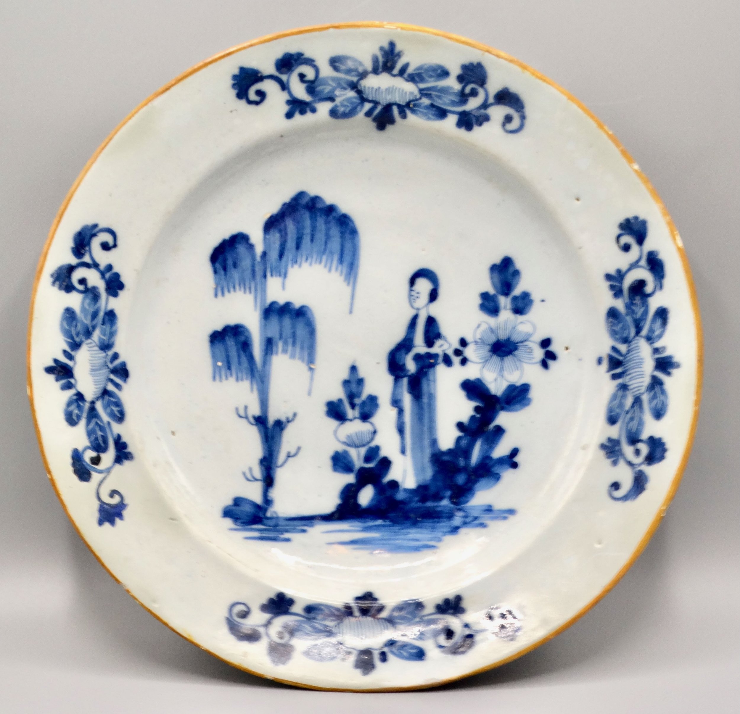 18th-century Dutch Delft figural charger “Lange Lijs” with hand painted blue design and orange edge.