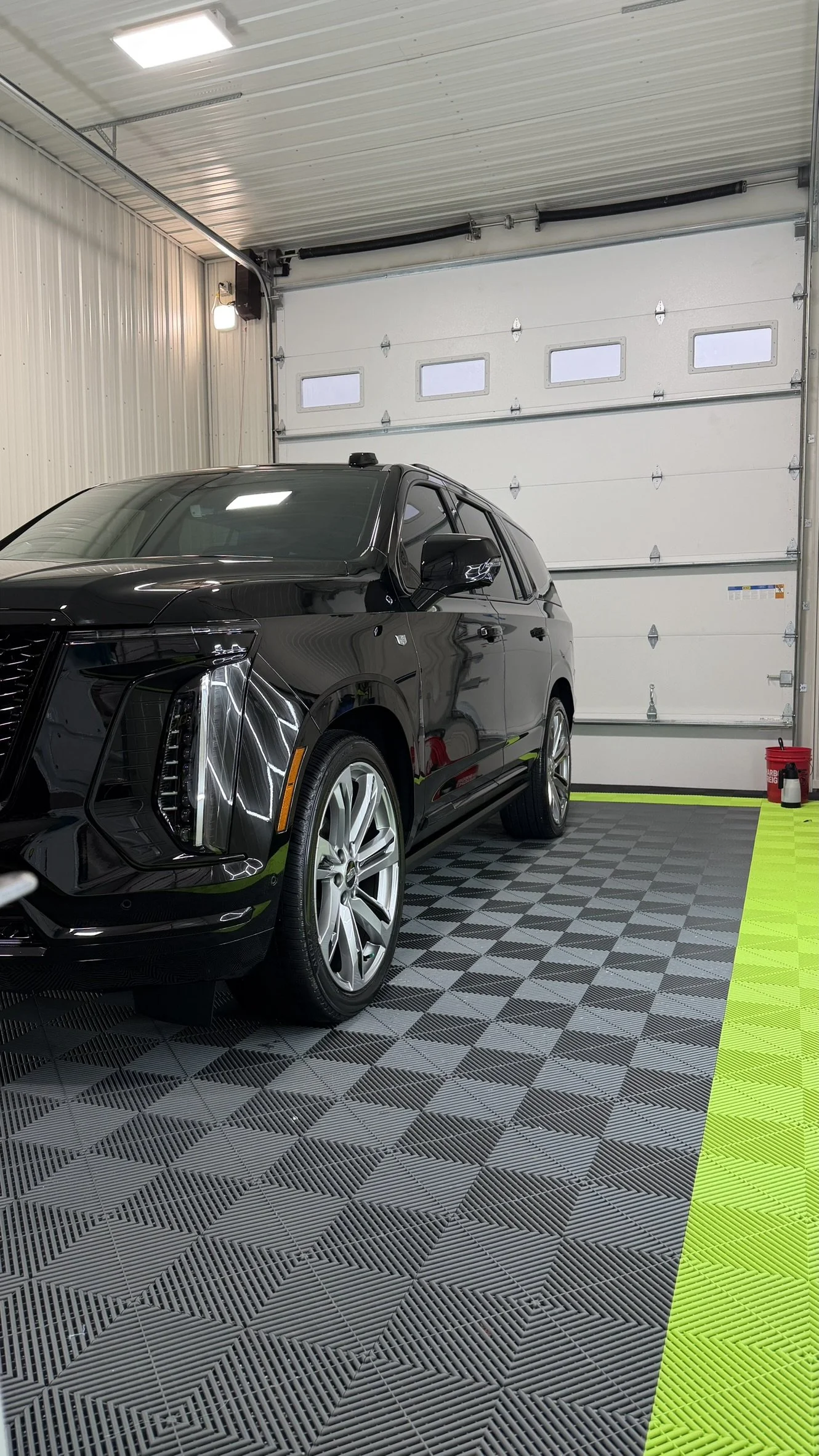 A black luxury SUV parked inside a well-lit, indoor garage with a patterned rubber floor and a white garage door.