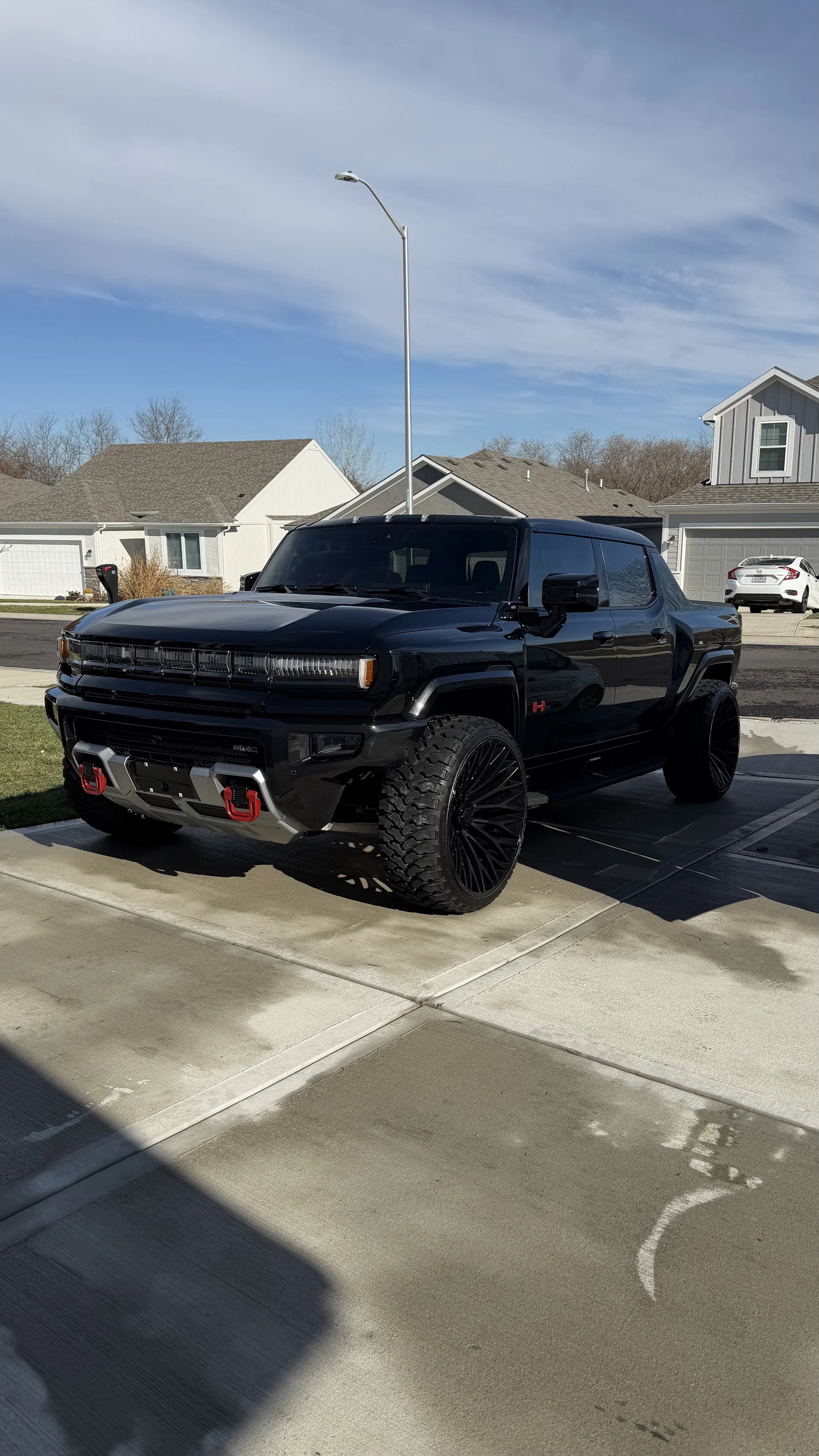 Black pickup truck with custom large black wheels, parked in a suburban driveway on a clear day.