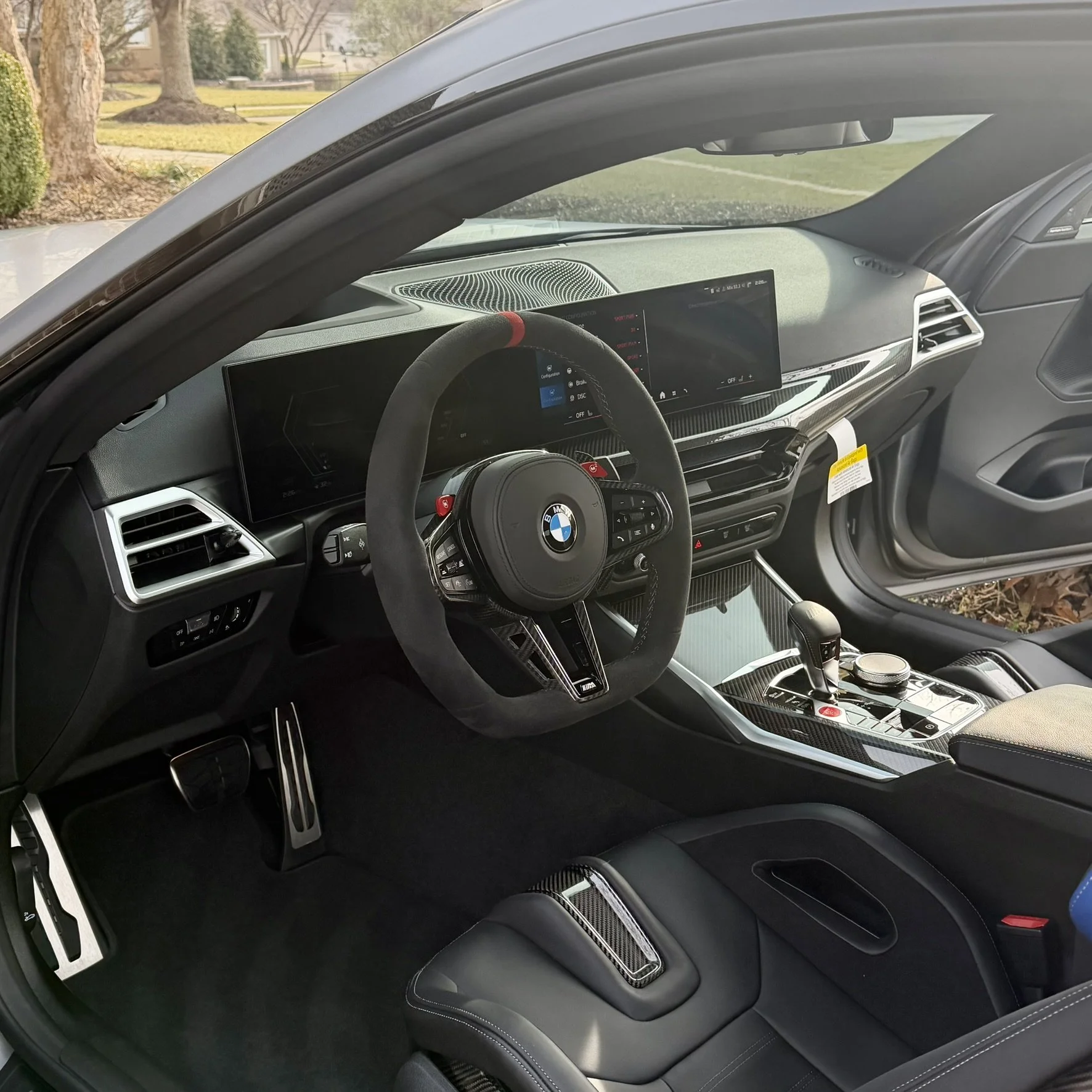 Inside the driver's seat of a BMW car showcasing a modern digital dashboard, steering wheel, gear shifter, and center console with electronic controls.