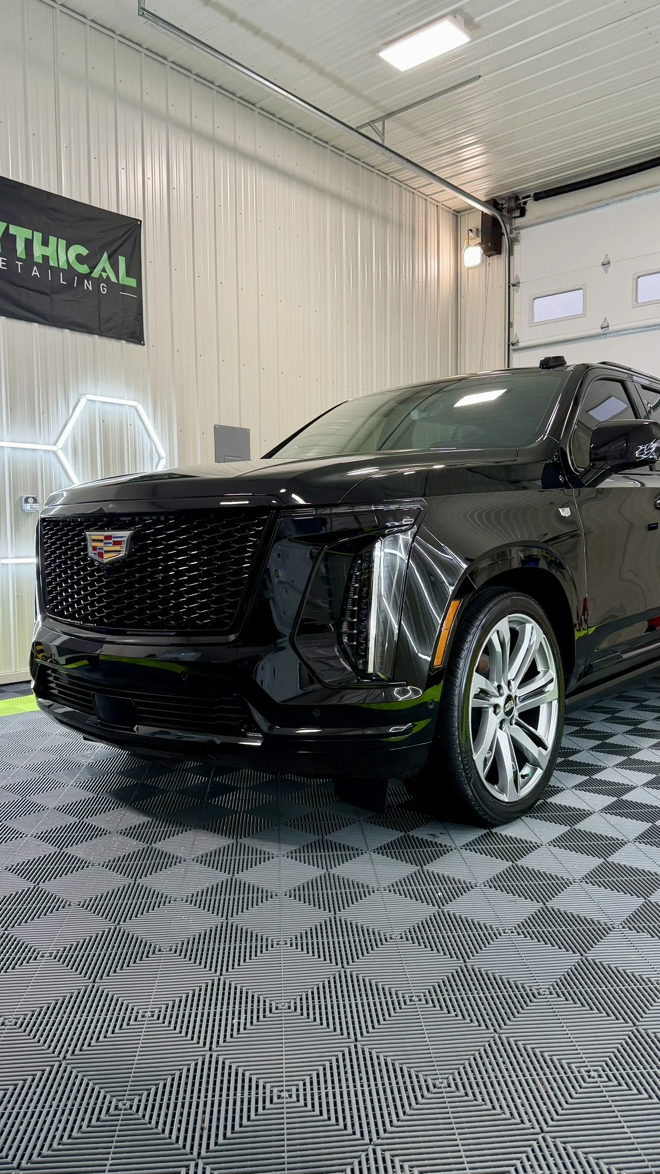 Black Cadillac SUV inside a garage with gray patterned flooring and white metal walls.