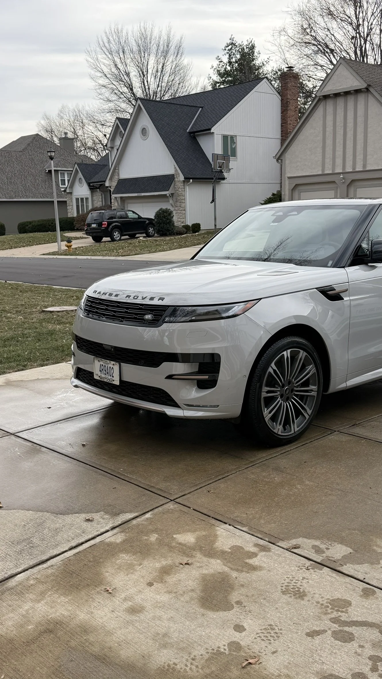 A white Range Rover SUV parked on a concrete driveway in front of a suburban house on a cloudy day.