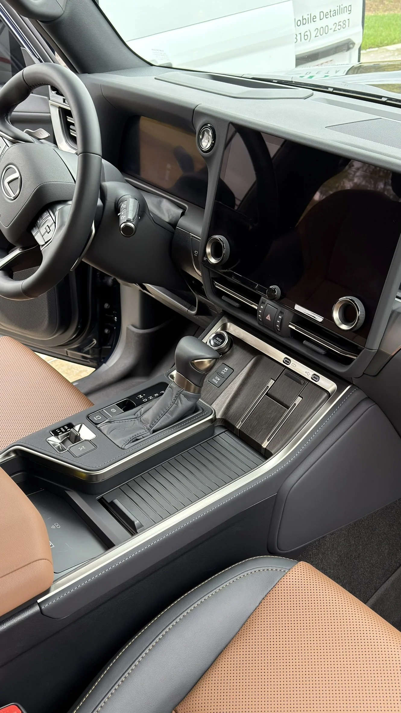 The interior of a modern Lexus vehicle, showing the steering wheel, large digital display screens, gear shift, and center console with various control buttons.