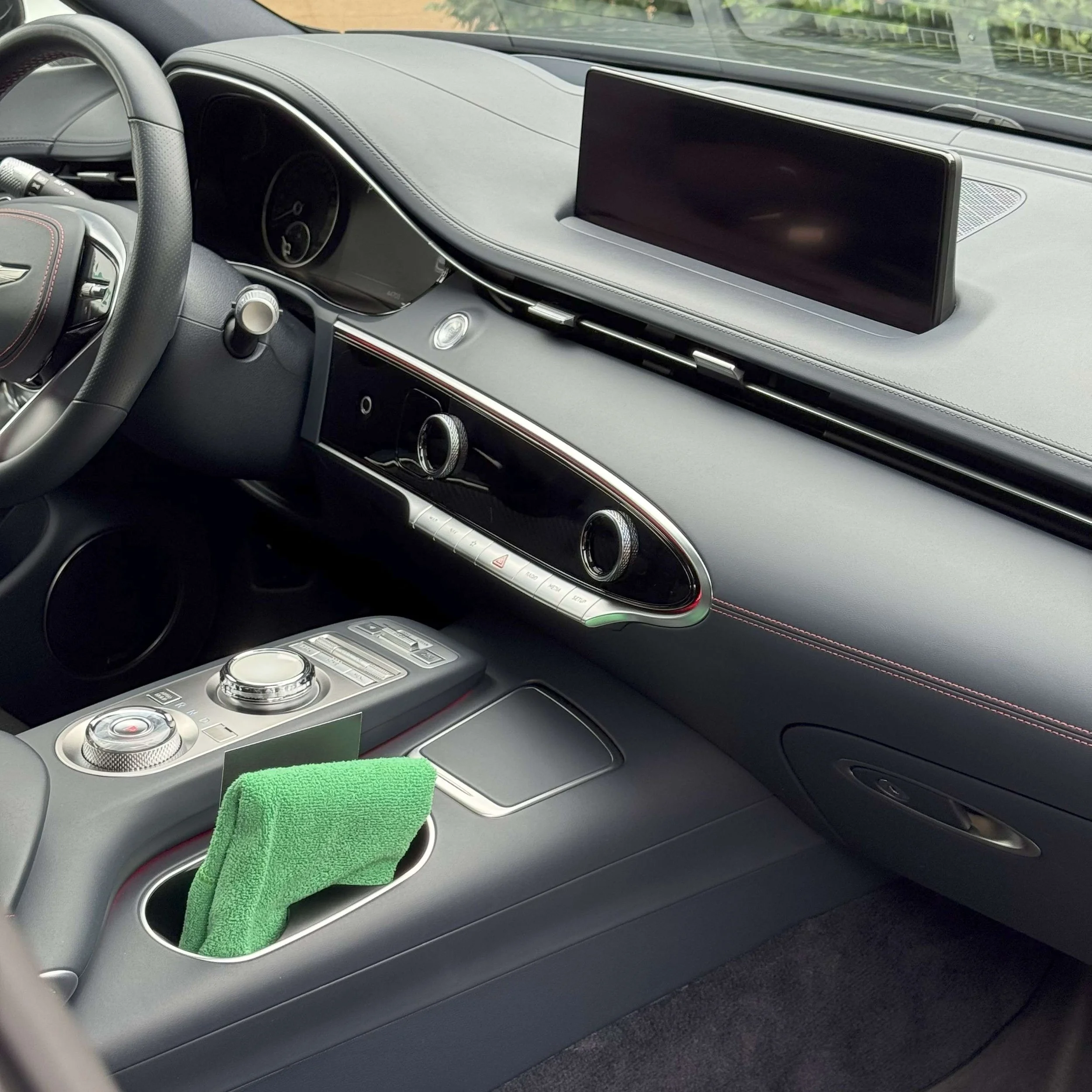 Interior of a luxury car dashboard with a large display screen, climate controls, and a green cloth inside a cup holder.