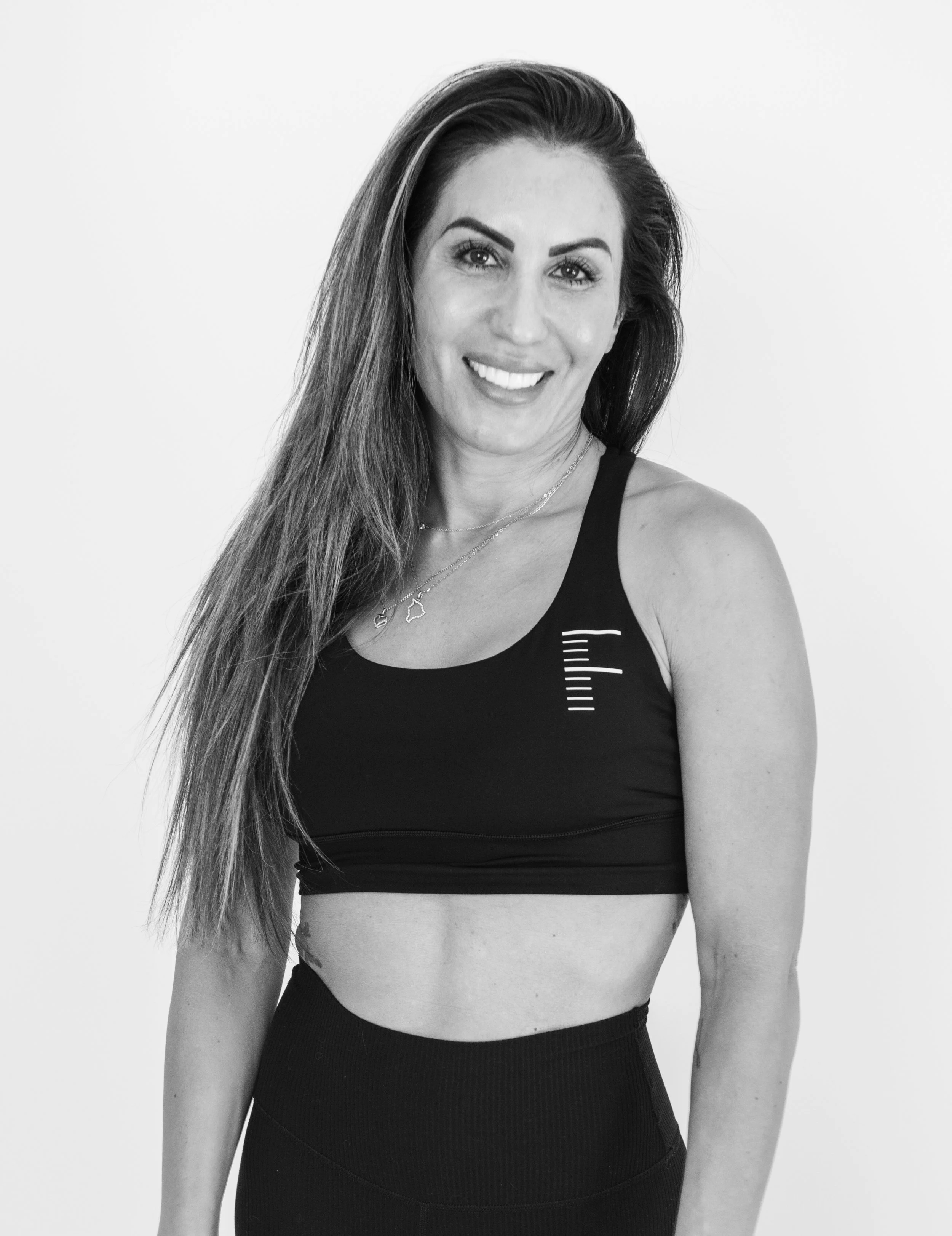 Black and white photo of a smiling woman with long hair wearing a sports bra and leggings.