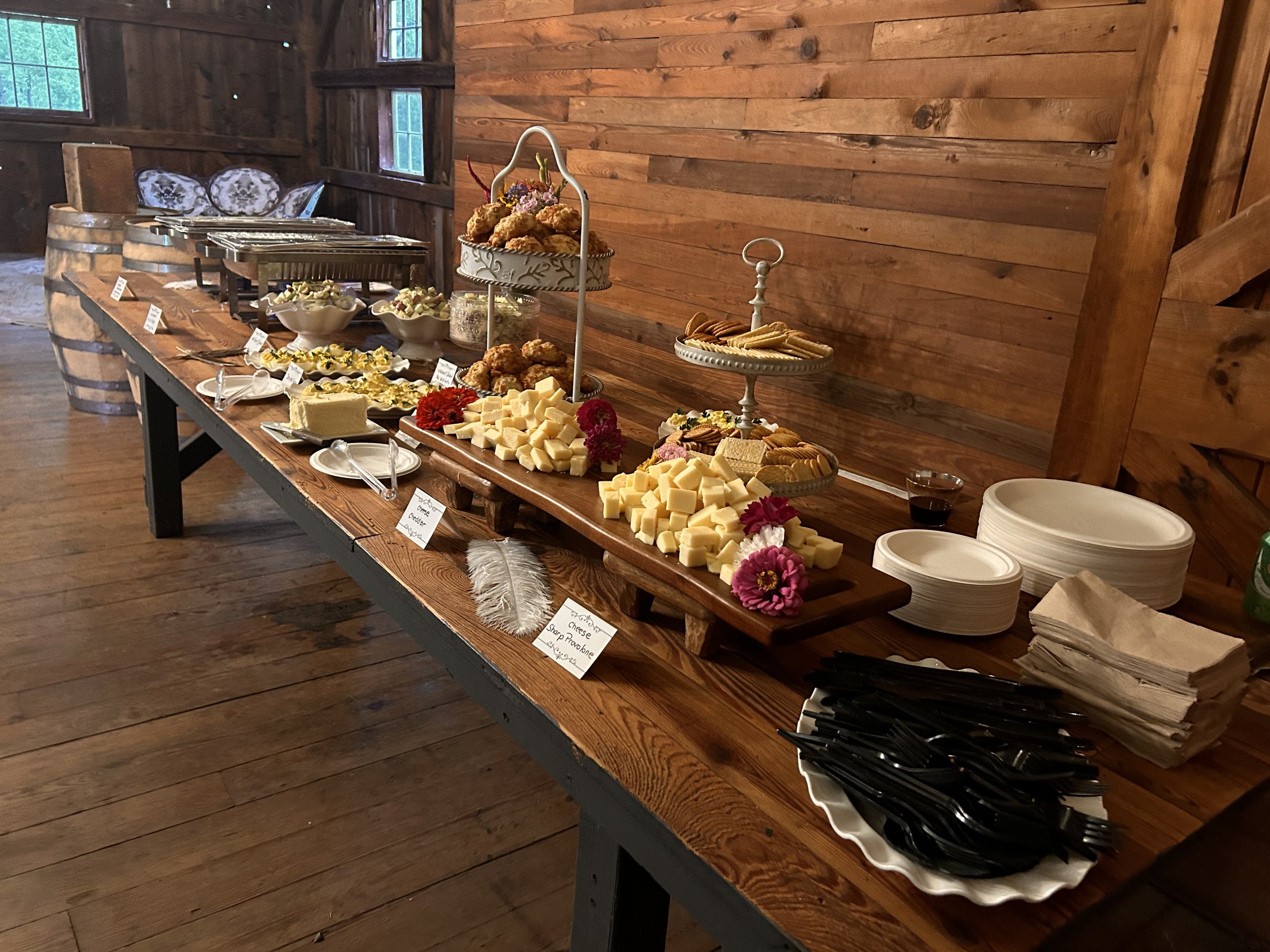 Buffet table with various appetizers in a rustic setting, featuring cheese cubes, deviled eggs, pastries, crackers, and plates.
