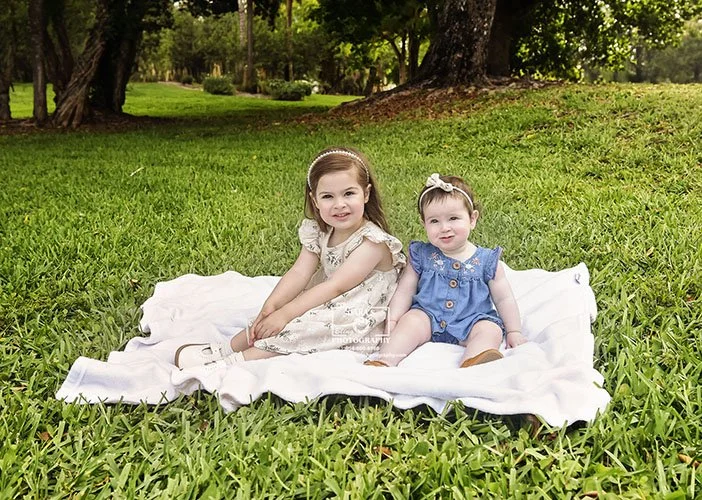 sibling photoshoot with sisters sitting on a blanket outside