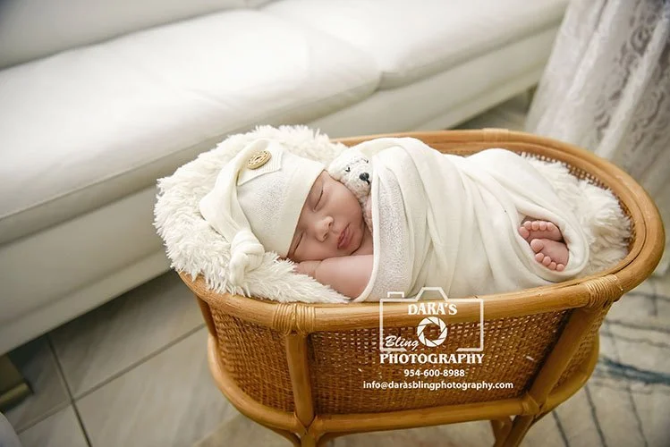 in home newborn photographer baby in a white wrap and white sleepy hat holding a bear posed in a wicker planter