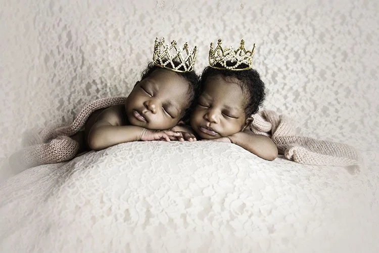 twin newborn girls posed on fabric wearing crowns