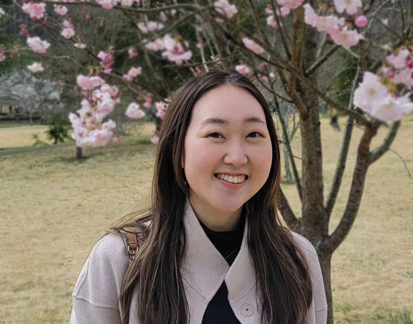 Julie Kim smiling in front of blooming cherry blossoms in a park.