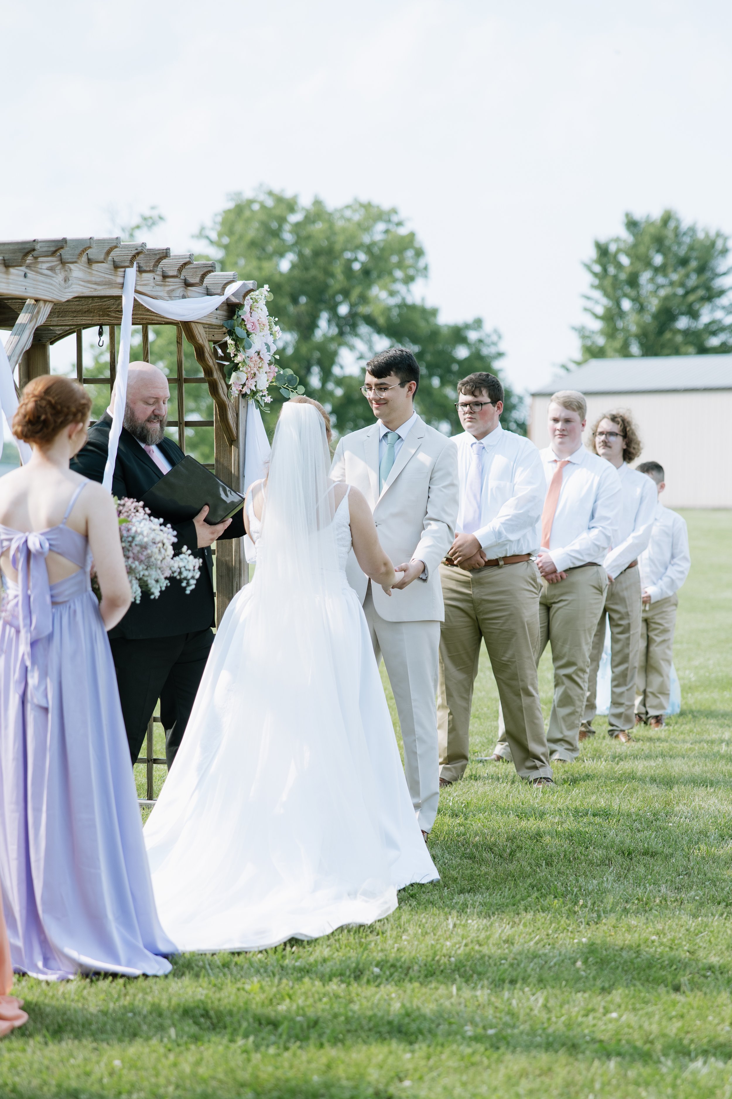 A couple getting married outdoors with a wedding officiant and bridesmaids and groomsmen standing nearby.