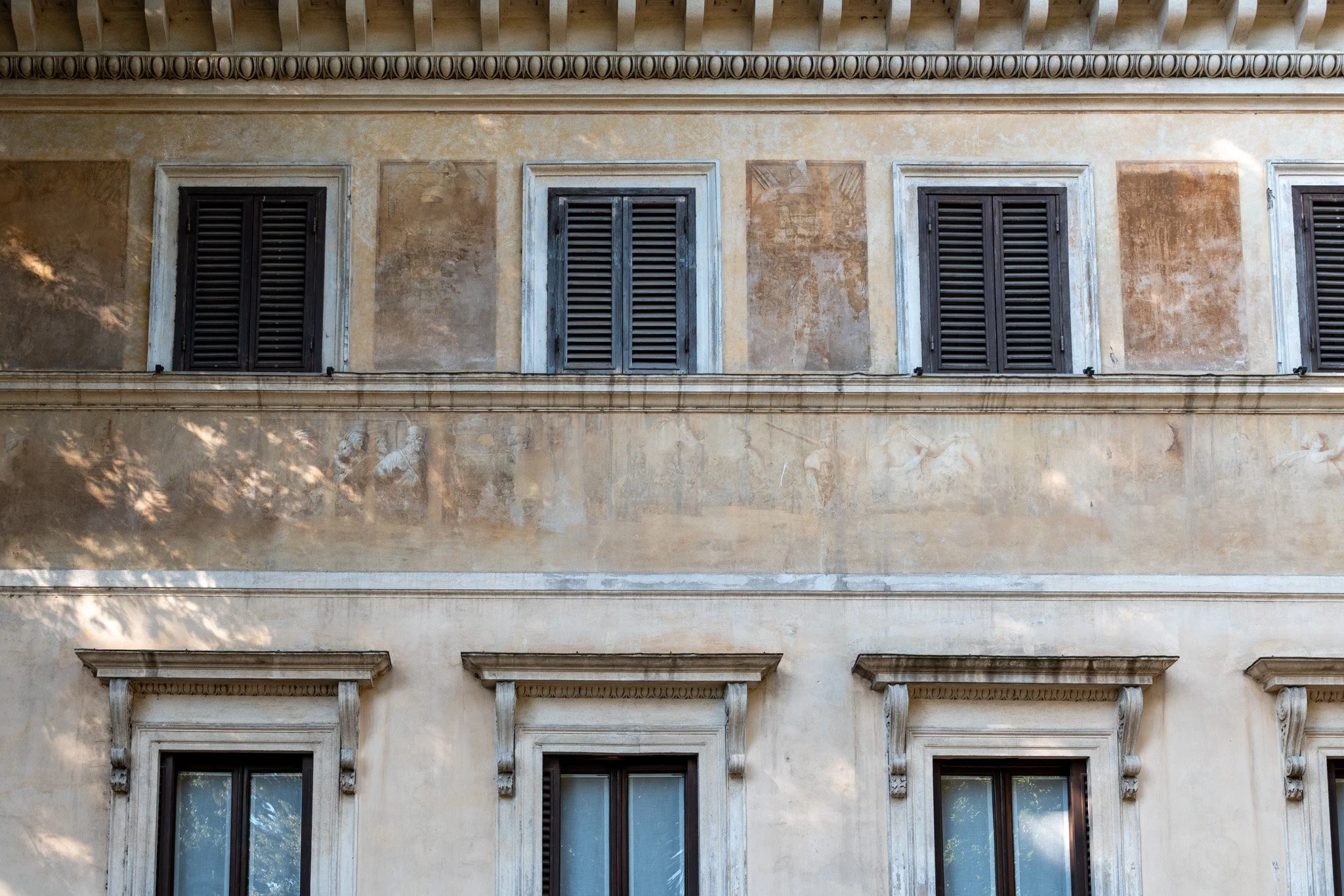 Weathered Rome building façade with three shuttered windows and pale stone trim, cropped in a calm horizontal band