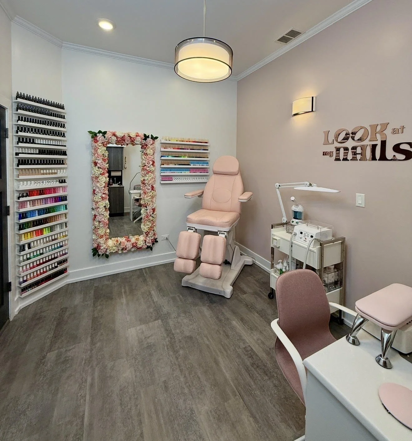 Interior of a beauty salon or nail salon with a treatment chair, a nail polish display wall, a mirror surrounded by flowers, and manicure tools.