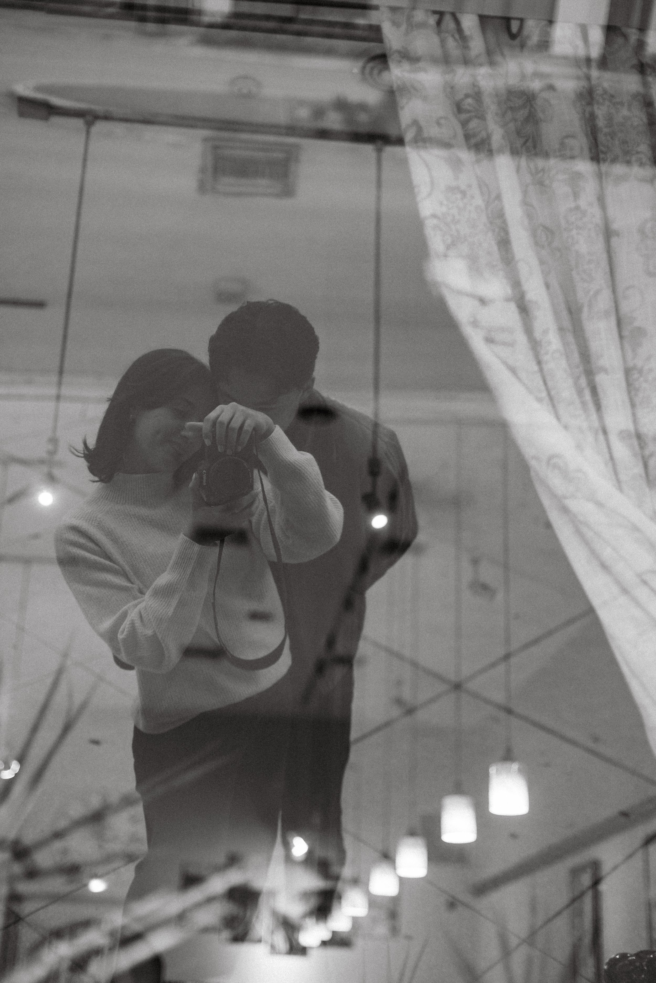 Couple embracing behind window curtain, quiet moment in documentary style wedding photography