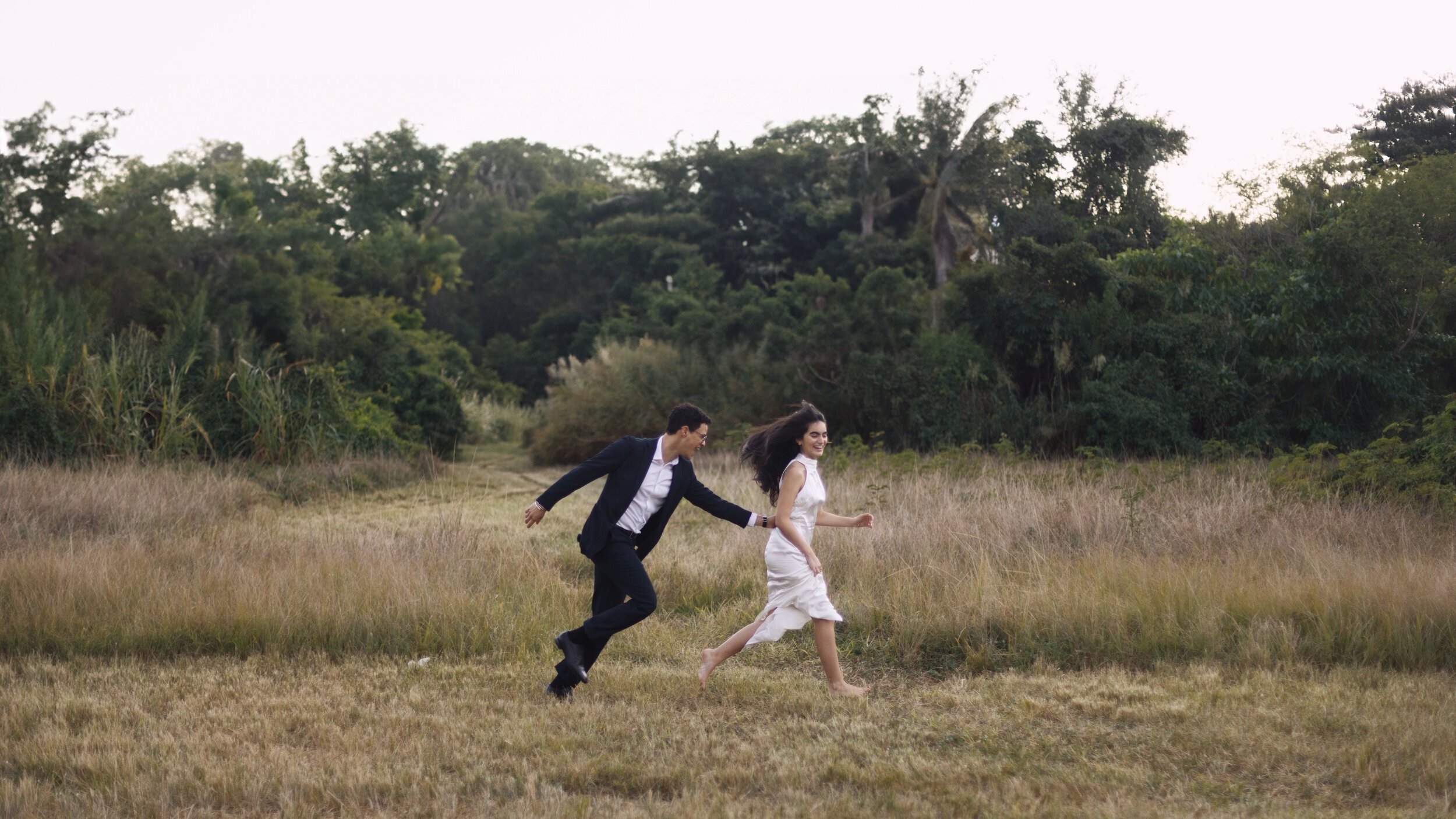 Couple running through open grassy field, candid moment in documentary style wedding photography
