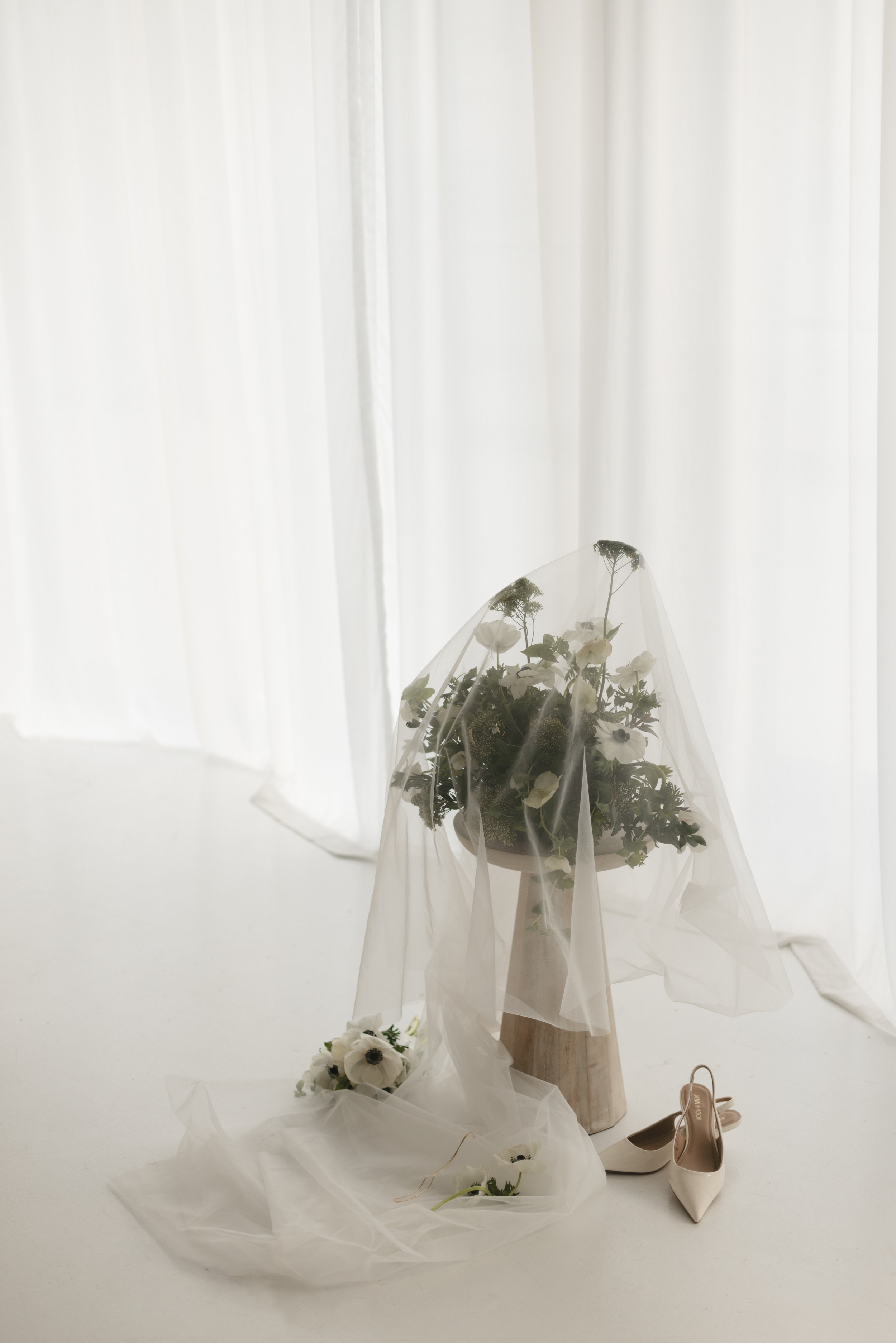 Bridal bouquet sits beneath sheer curtain, thoughtful still life in documentary wedding photography