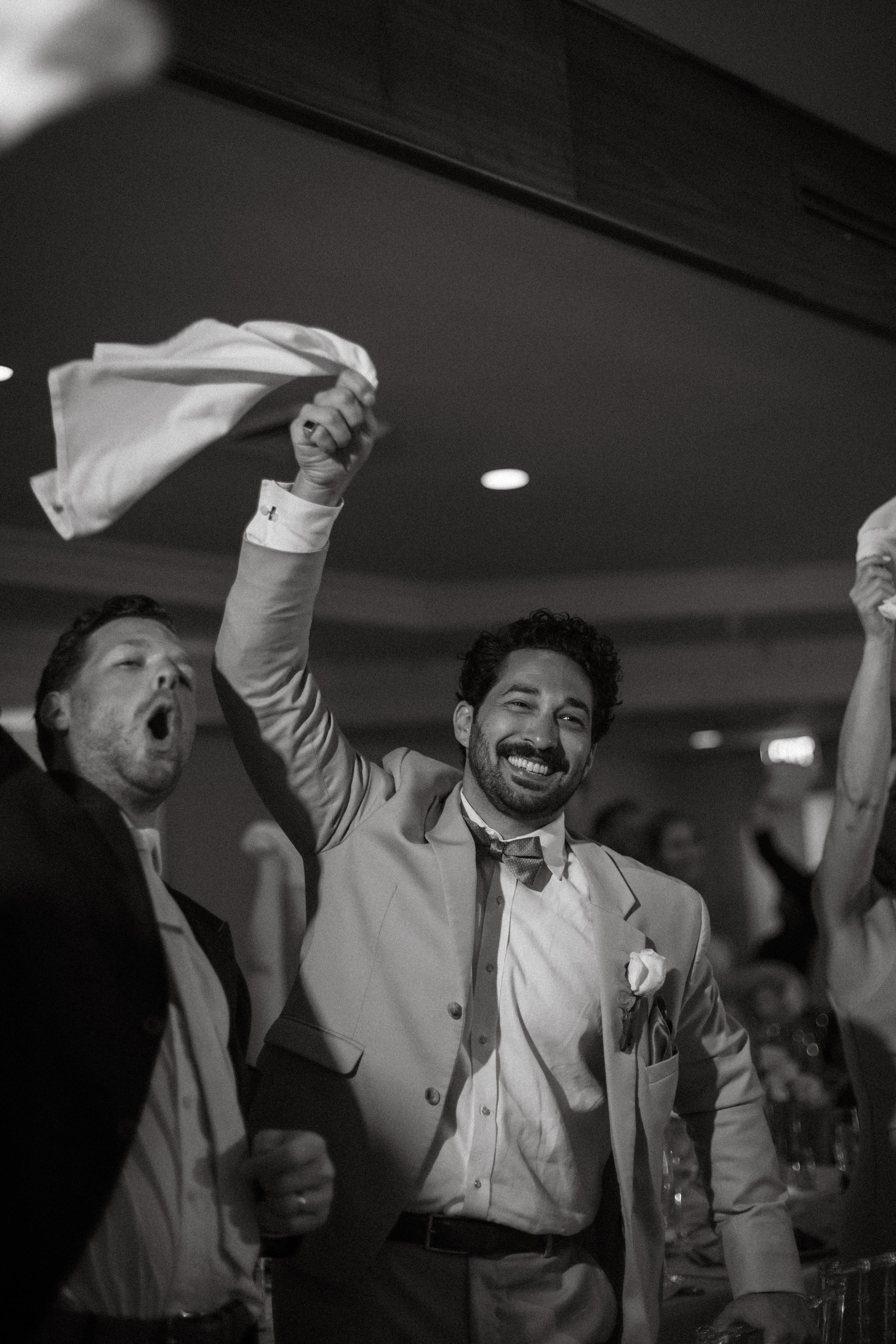 Groom waves napkin at reception, celebratory energy in documentary style wedding photography
