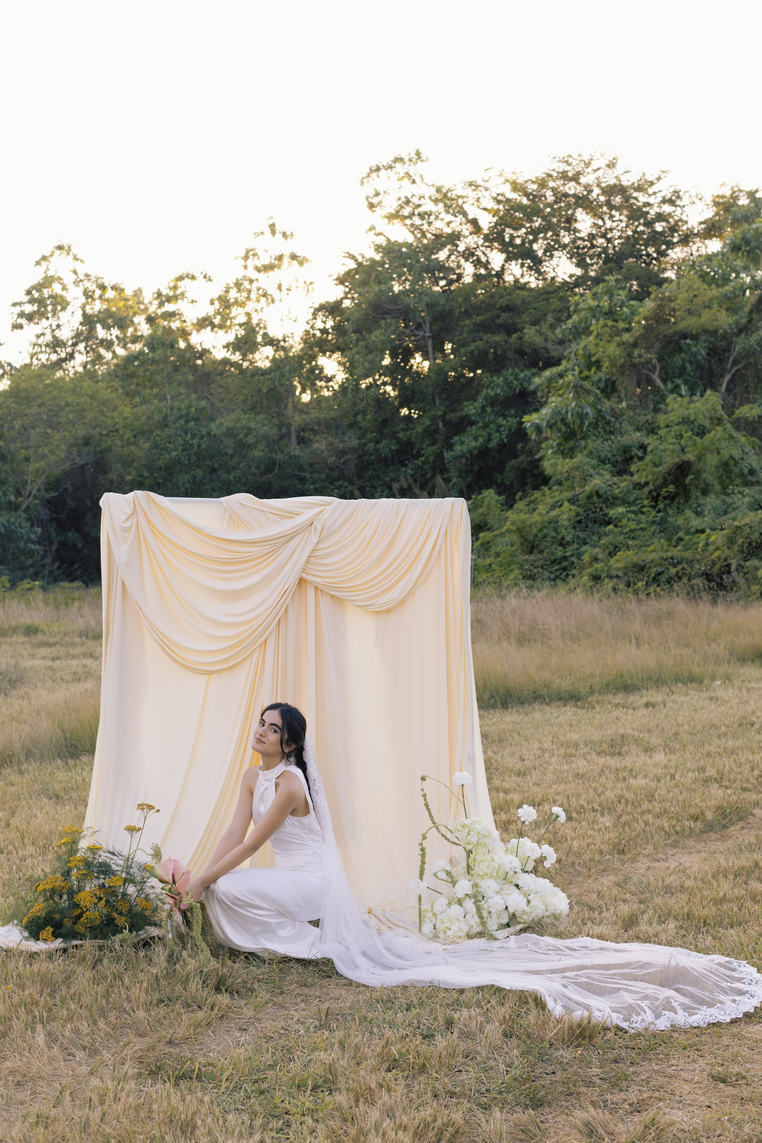 Bride sits under peach draped altar, outdoor scene in documentary style wedding photography
