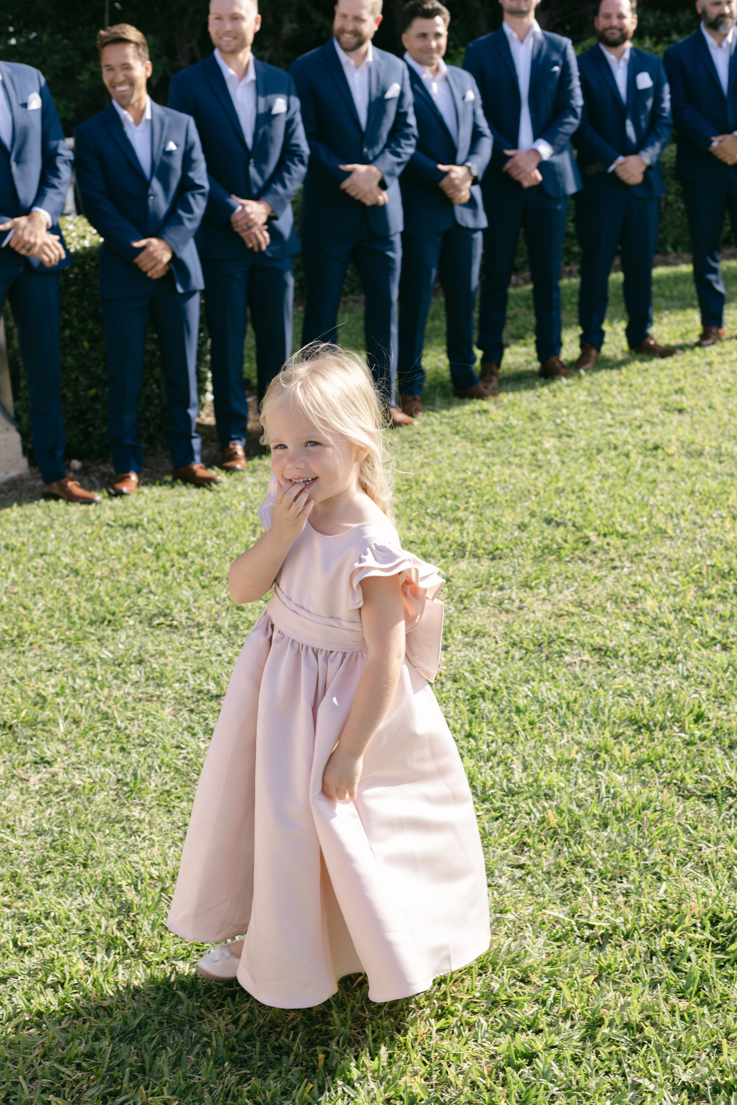 Flower girl stands on ceremony lawn, sweet moment in documentary wedding photography