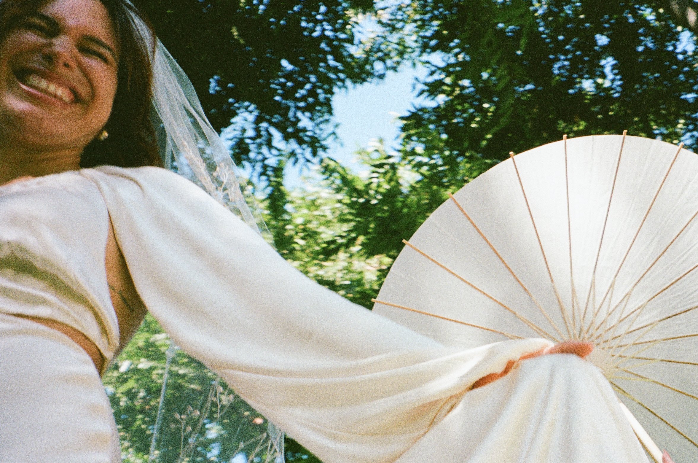 Bride holds parasol beneath trees, documentary style wedding photography