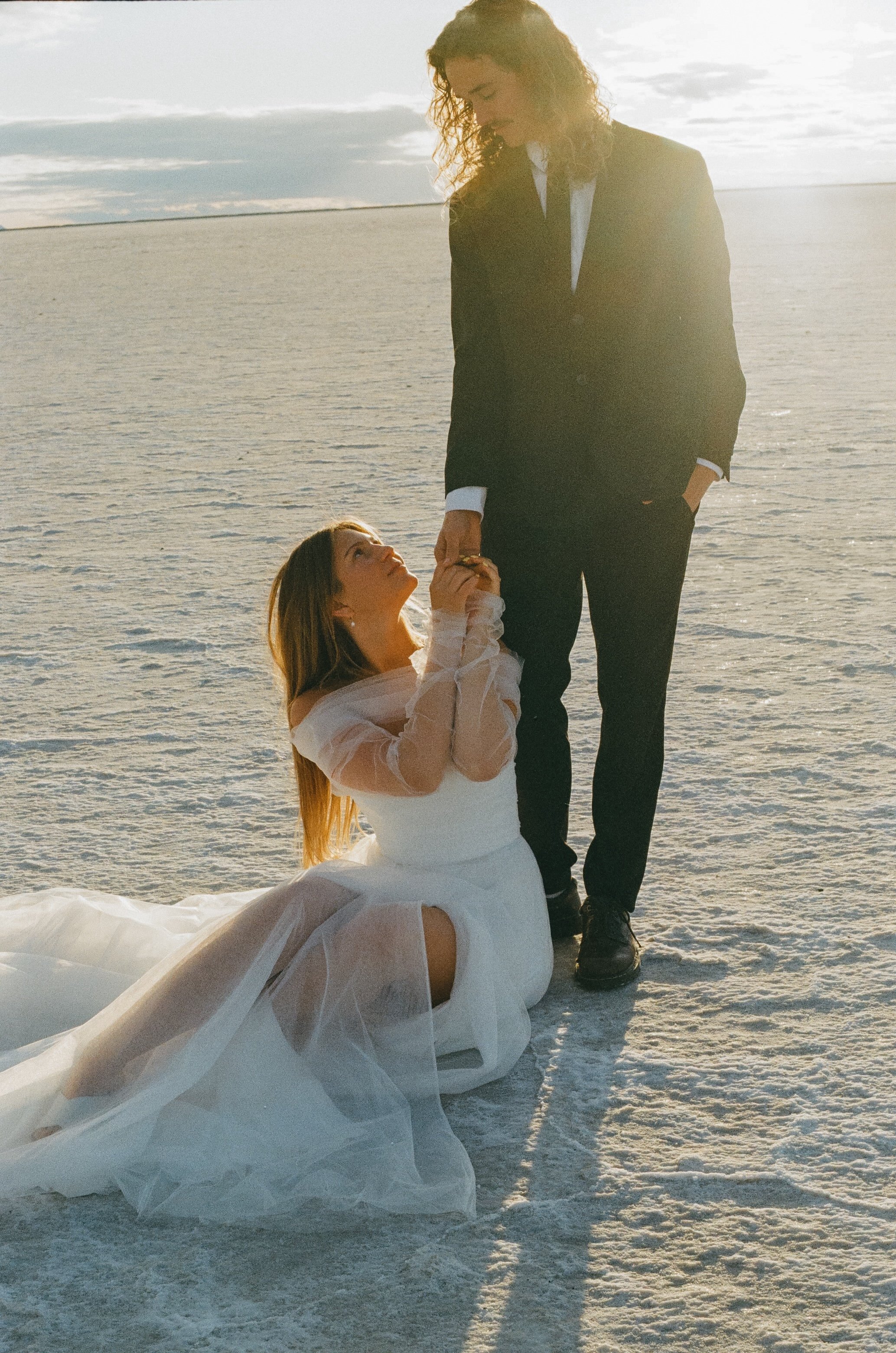 Bride kneels holding groom’s hand, captured in documentary wedding photography