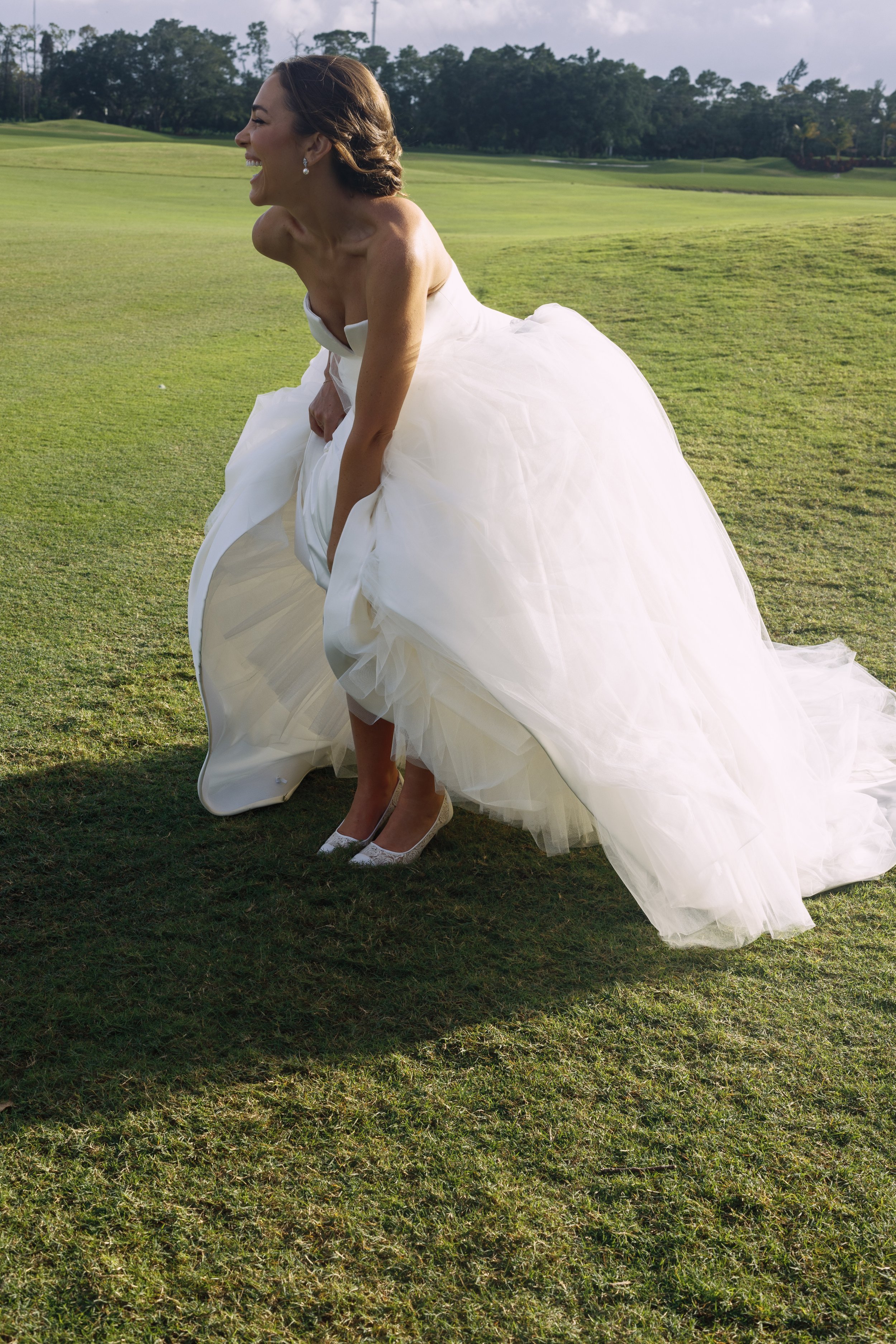 Bride holding dress, walking on lawn, joyful capture by documentary wedding photographer