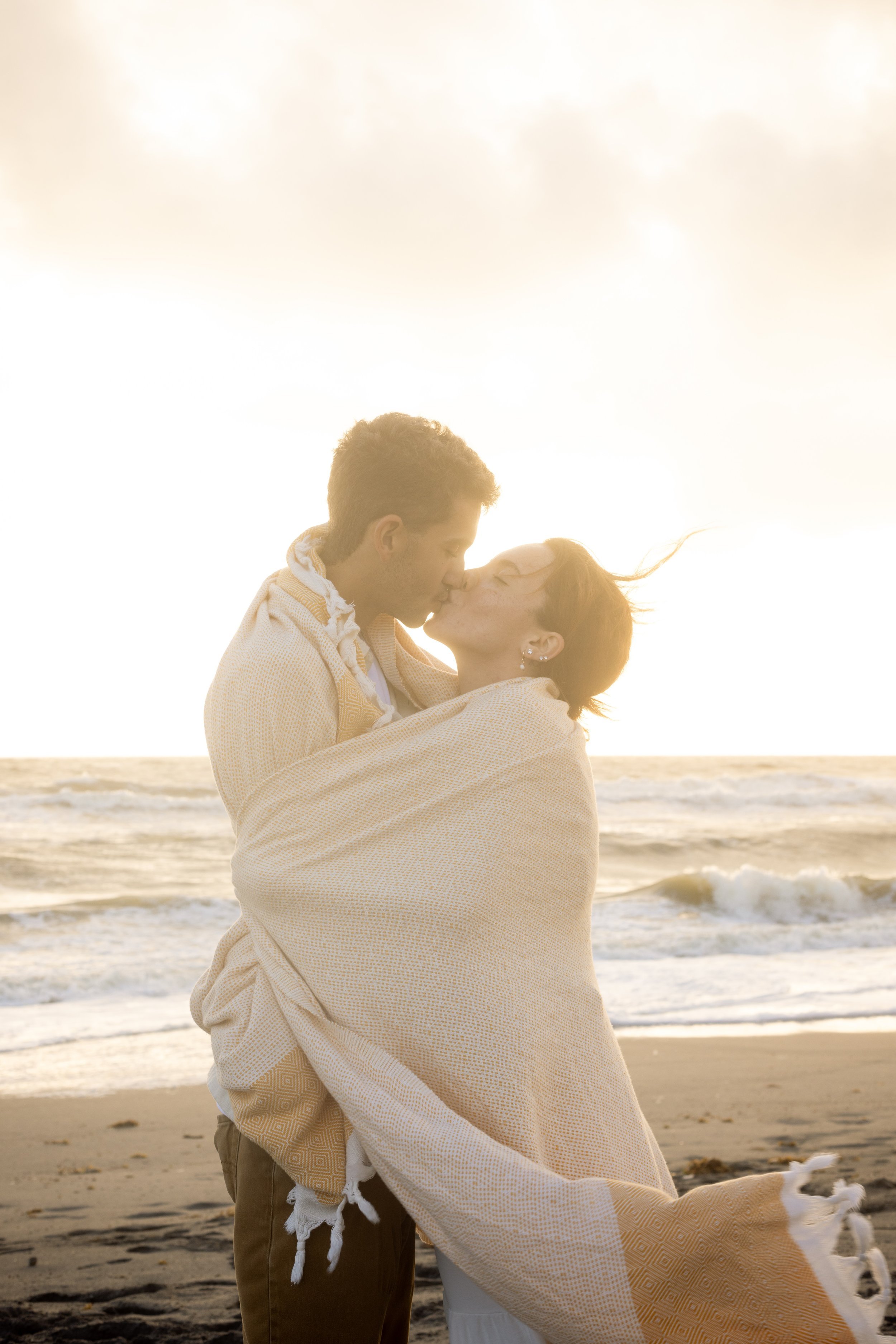 Couple wrapped in blanket at beach, captured by documentary wedding photographer
