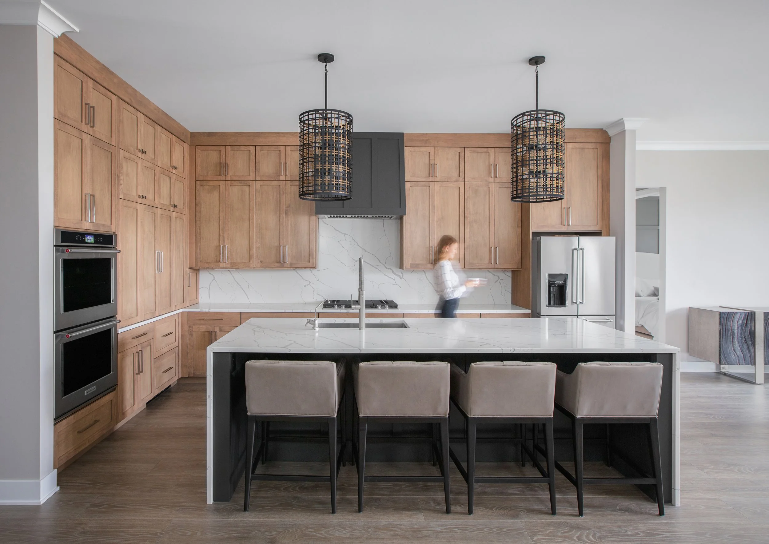 Contemporary kitchen in a DEV Partners real estate development, featuring natural wood cabinetry, marble countertops, and modern black pendant lighting. A woman moves gracefully in the space, illustrating the benefits of real estate investment