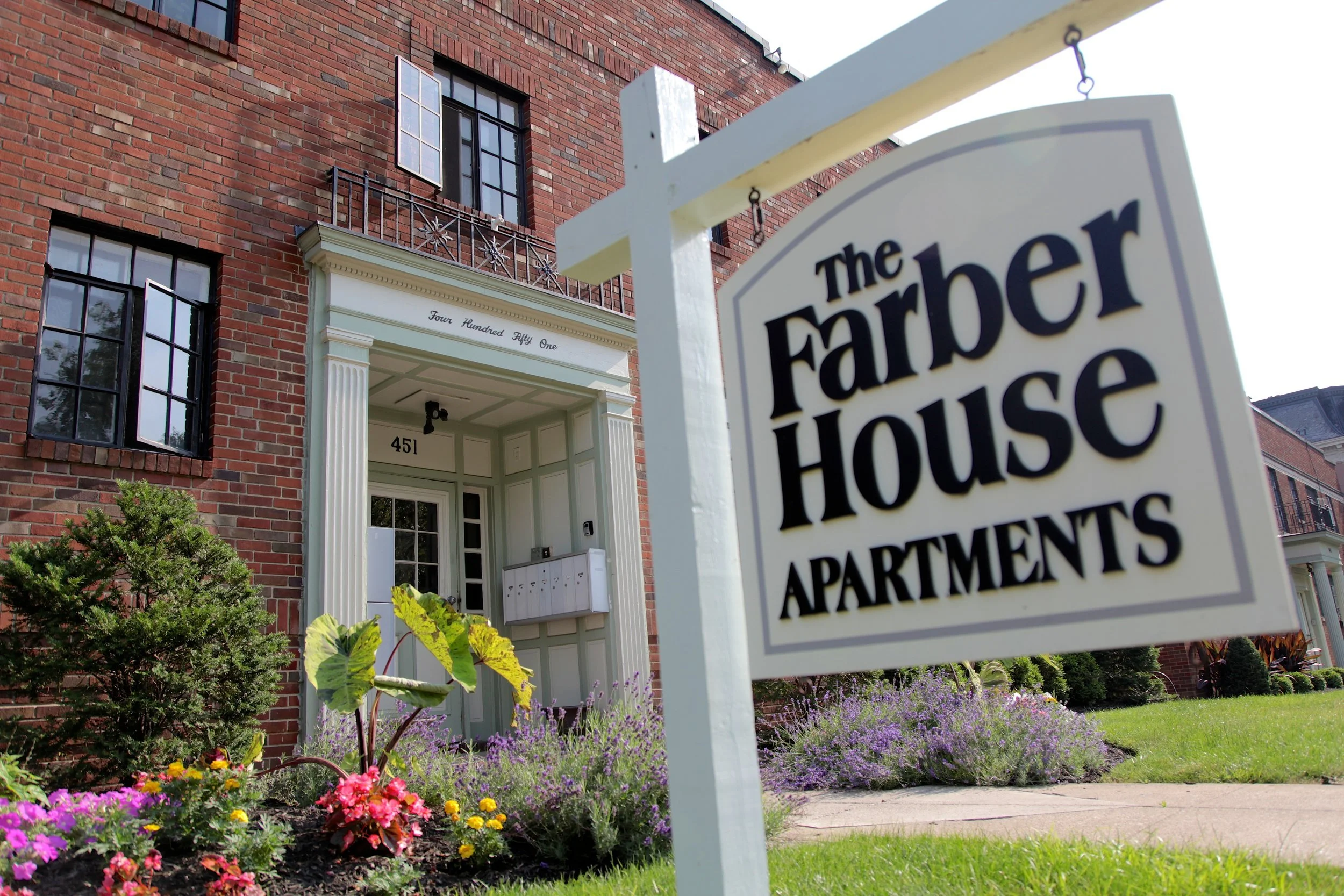 Exterior view of The Farber House Apartments in downtown Columbus, Ohio, a charming multi-family property offering passive income rentals, managed by DEV Partners, featuring a red brick facade, decorative shutters, and a well-landscaped entrance.